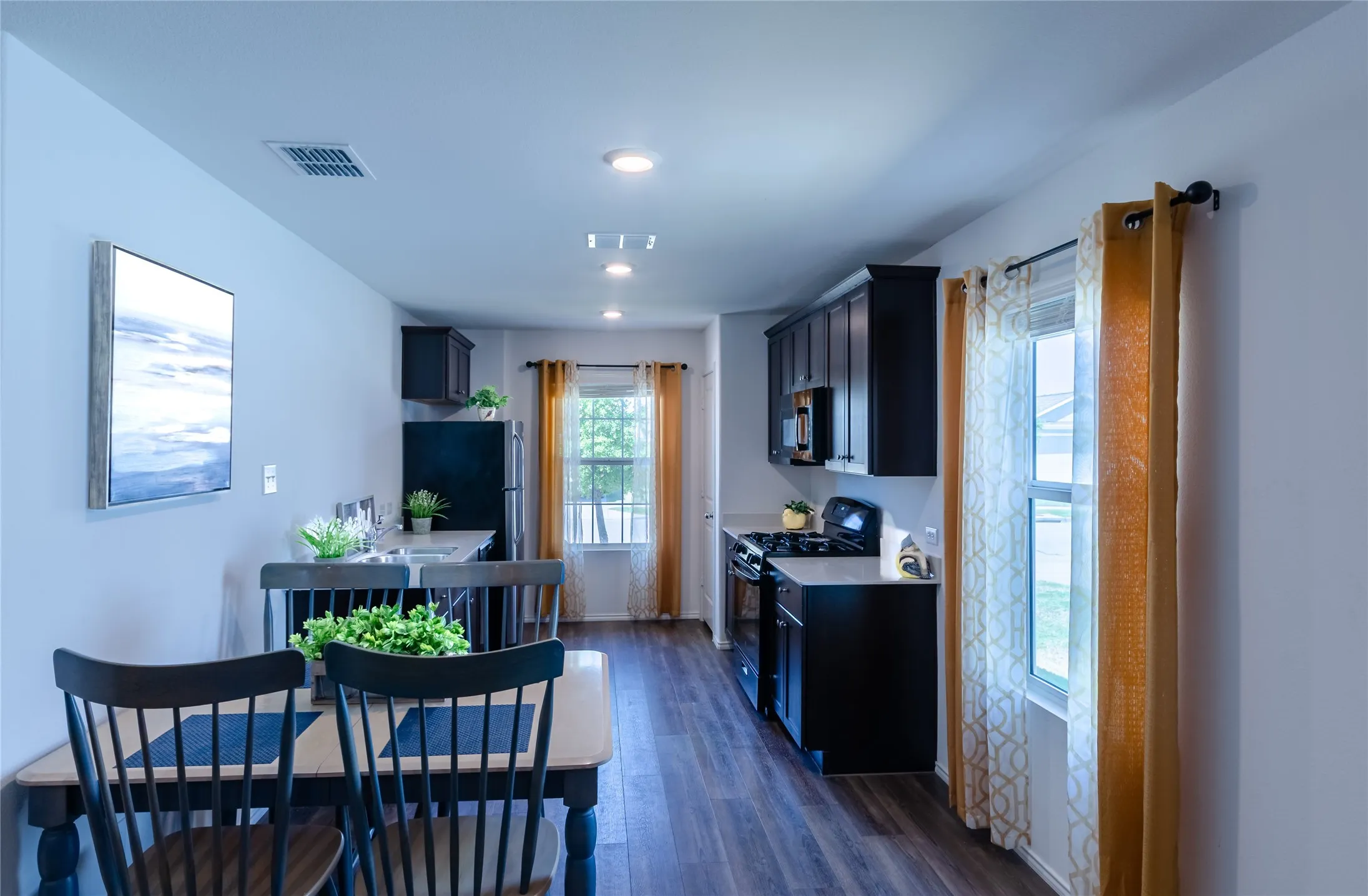 Kitchen featuring dark wood-finish cabinetry, black appliances, light-toned countertops, and wood-finish flooring
