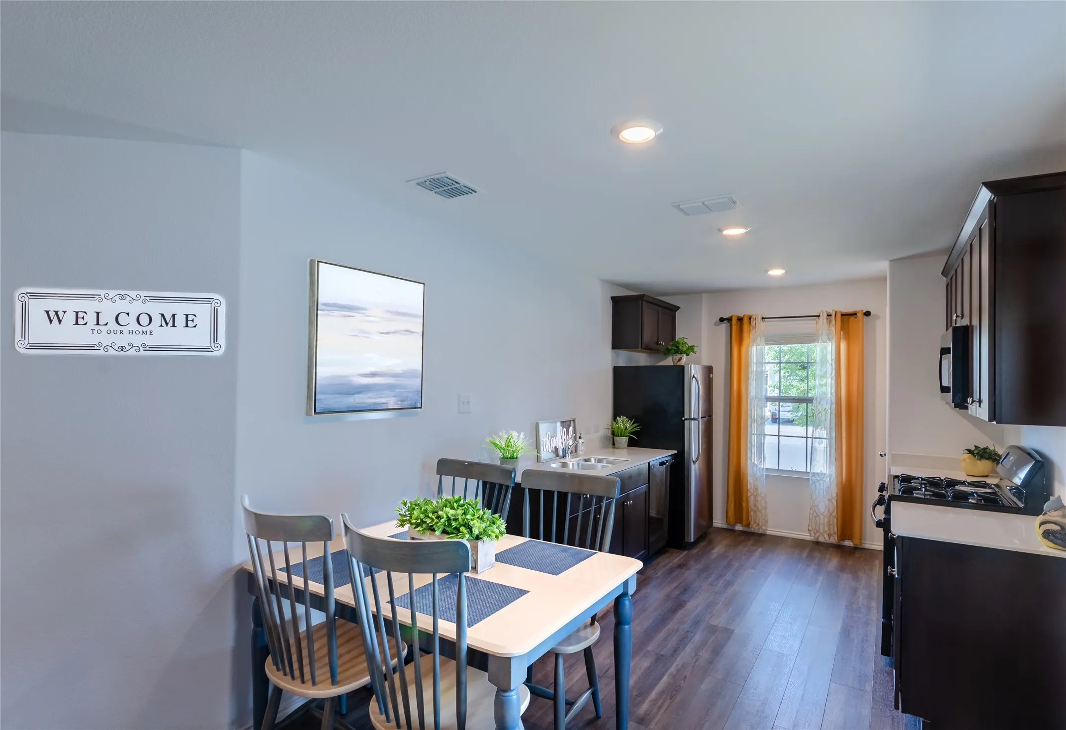 Open-concept living space with dark wood-finish flooring, recessed lighting, and a kitchen featuring dark cabinetry, stainless steel appliances, and a window for natural light