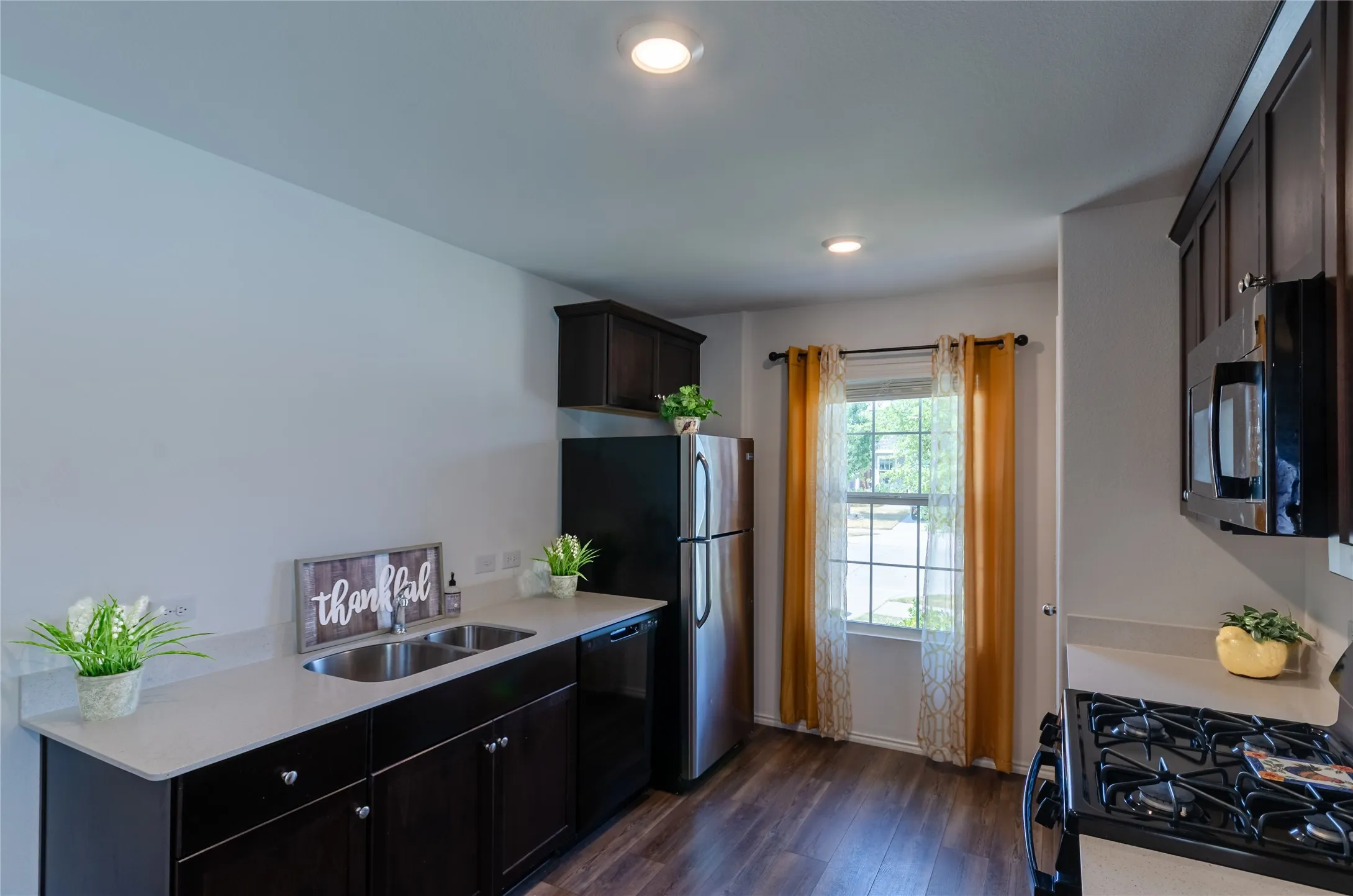 Well-appointed kitchen featuring wood-finish flooring, dark wood cabinetry, light-toned countertops, and stainless steel appliances
