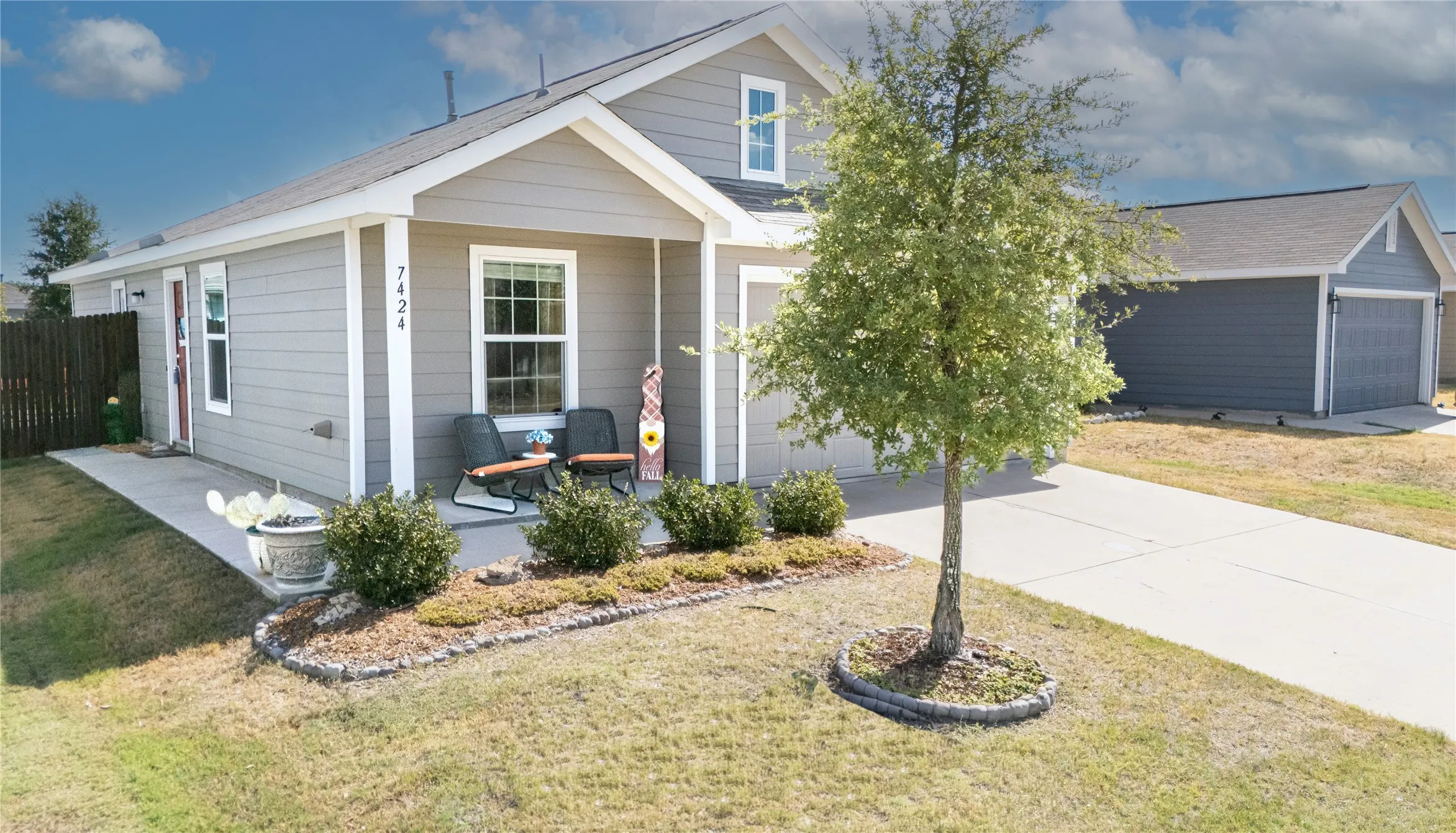 Covered front porch with decorative landscaping, concrete driveway, and attached garage
