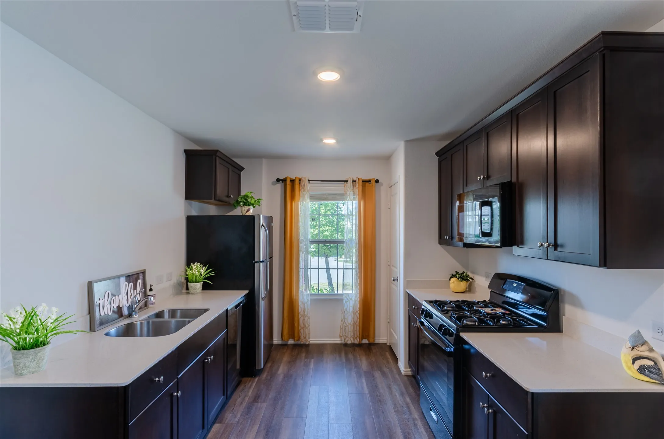 Galley kitchen with dark wood-finish cabinetry, light countertops, wood-finish flooring, and stainless steel sink
