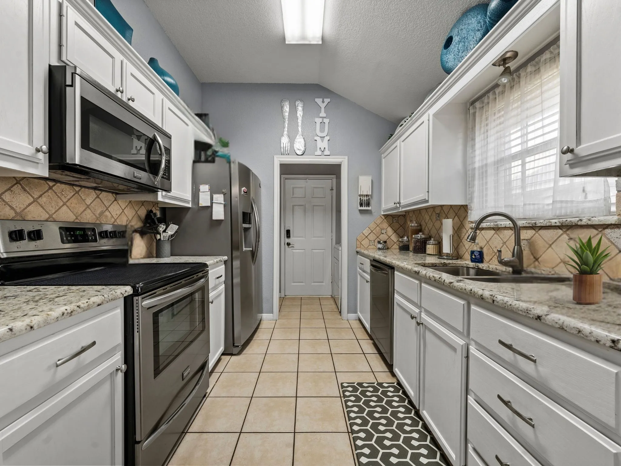 Galley kitchen featuring white cabinetry, granite countertops, stainless steel appliances, a tile backsplash, and tile flooring