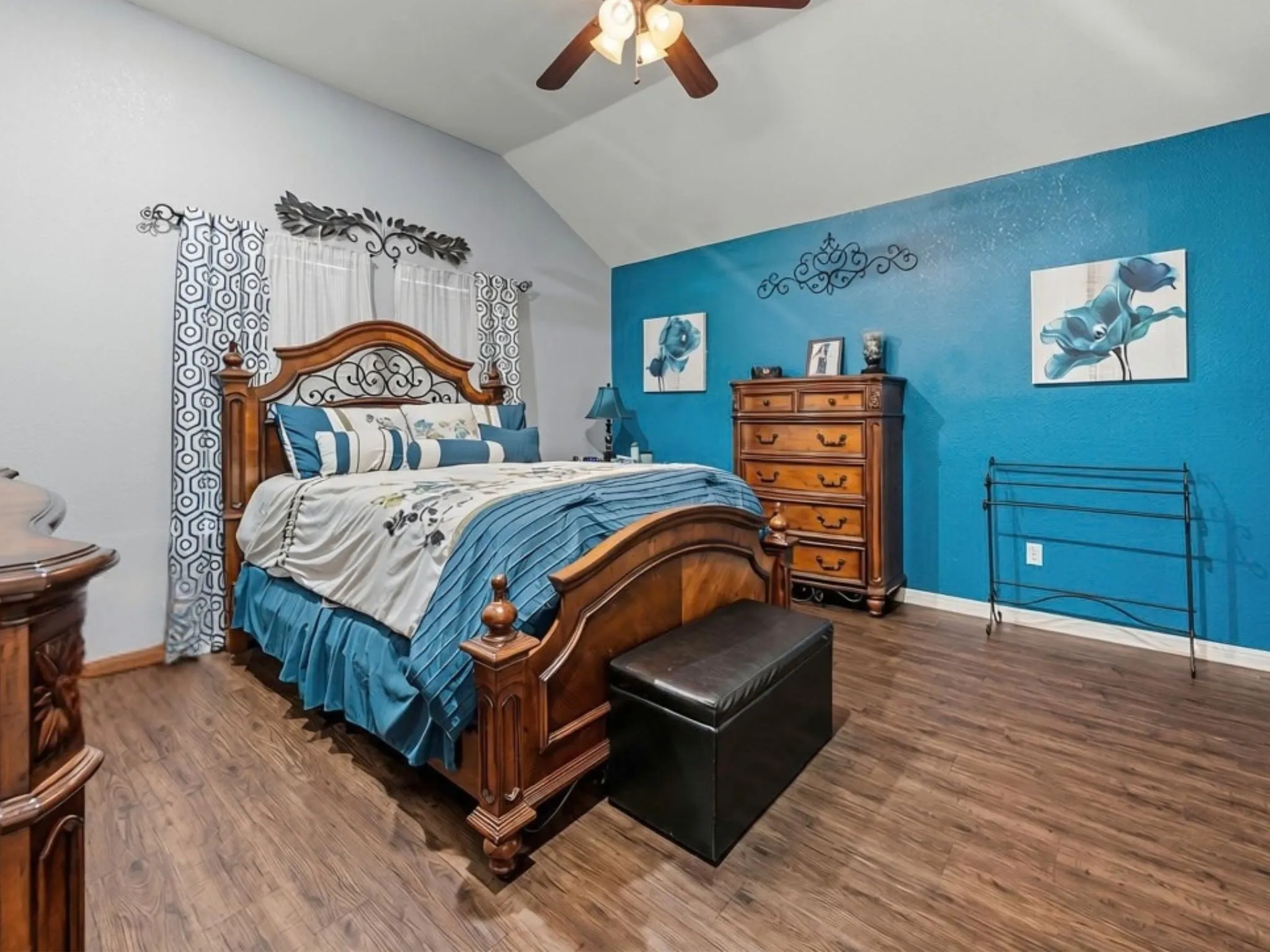 Vaulted ceiling with an attached ceiling fan, wood-finish flooring, and a decorative accent wall