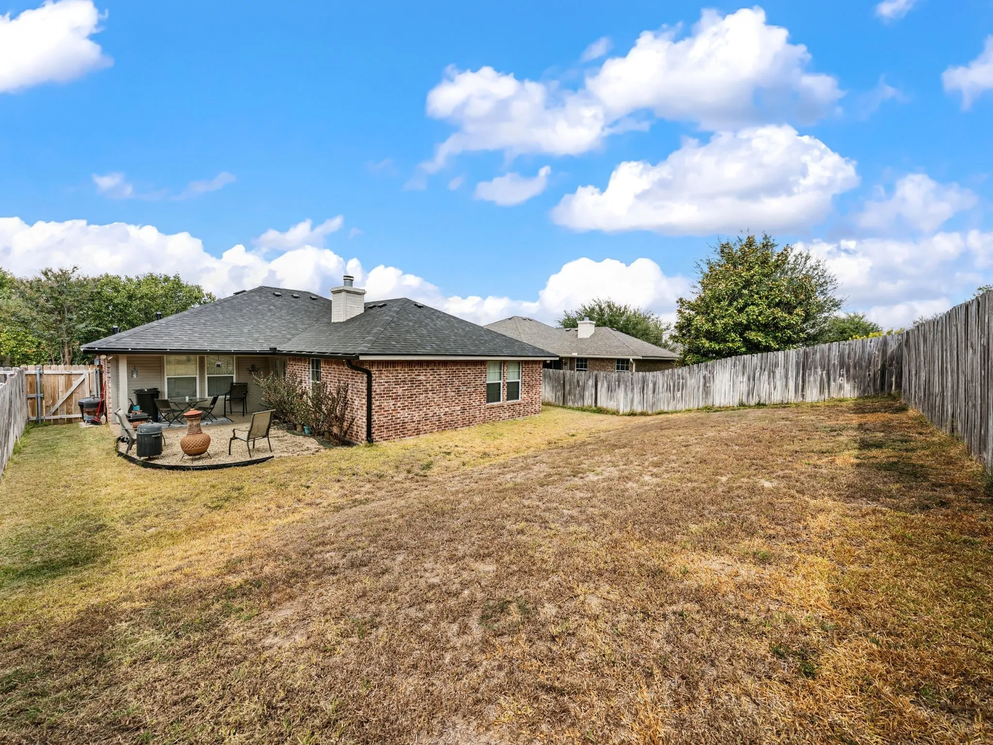 Brick exterior with a covered patio, a stone patio, and a wood privacy fence