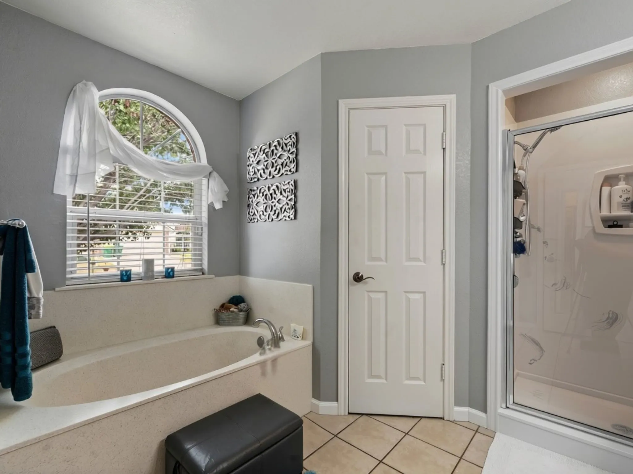 Garden tub with deck surround, arched window, privacy blinds, tiled flooring, and a stand-up shower enclosure