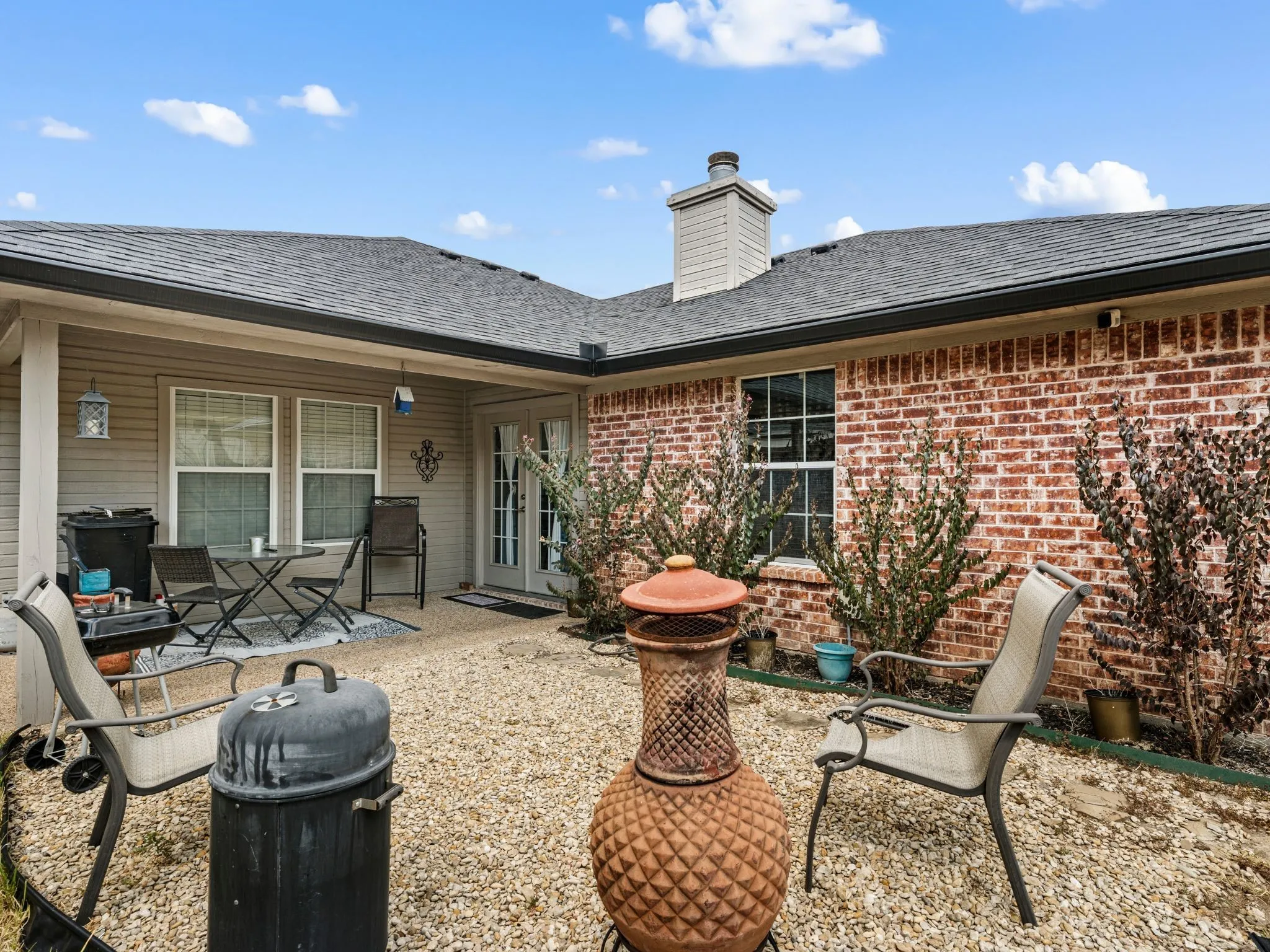 Brick exterior with shingle roofing, covered patio, white-framed windows, and French doors