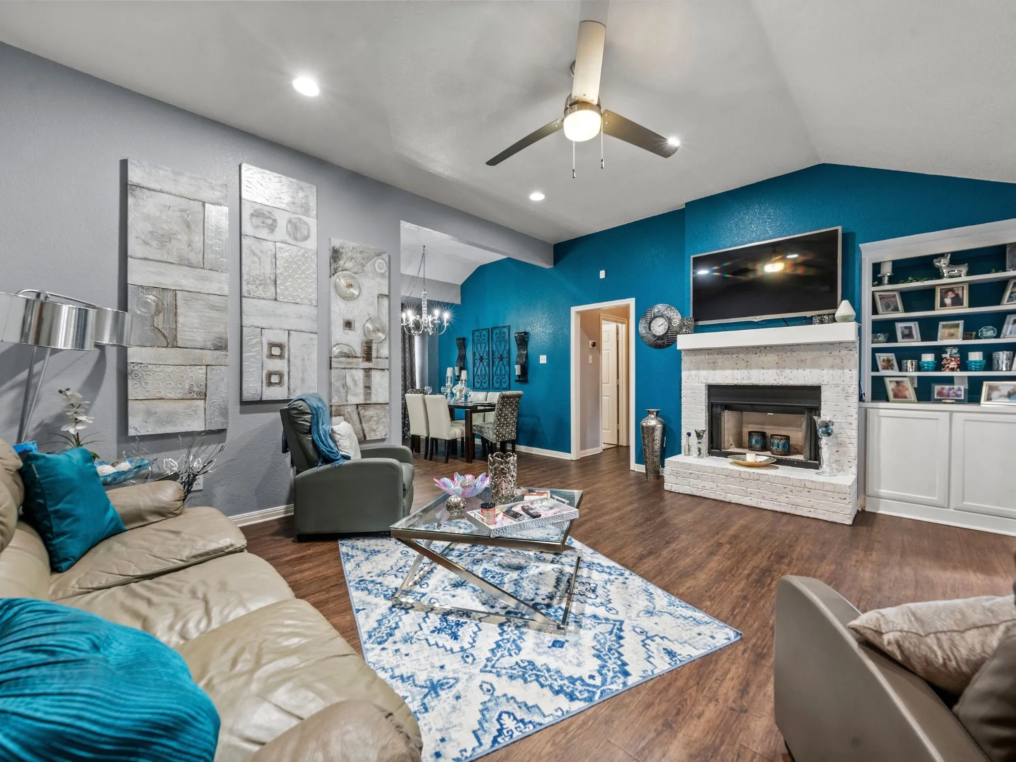 Vaulted ceiling with a ceiling fan, fireplace with a stone surround, built-in shelving and cabinetry, and wood-finish flooring