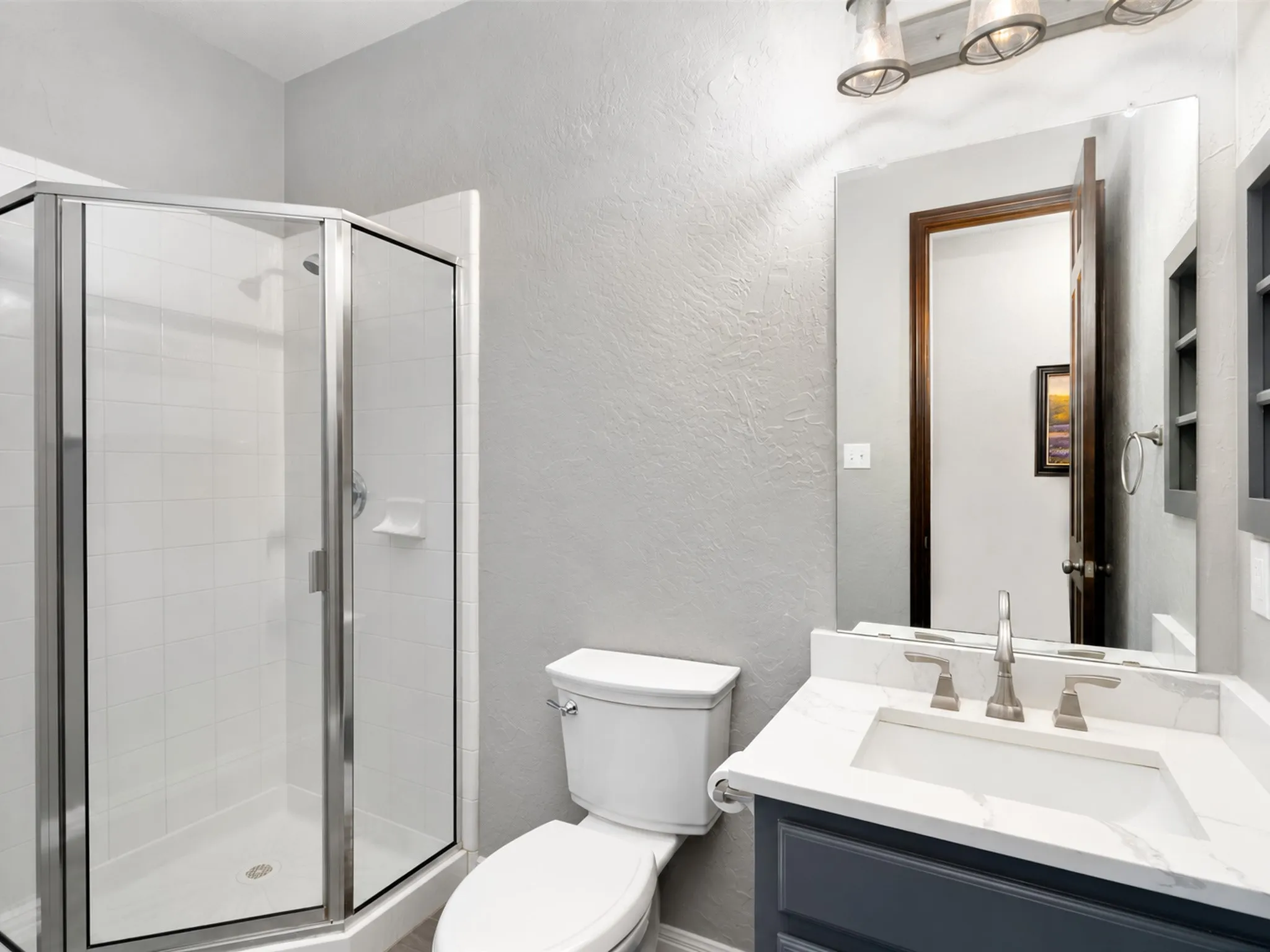 White tile shower enclosure with glass surround, vanity with light-tone countertop, and brushed nickel fixtures