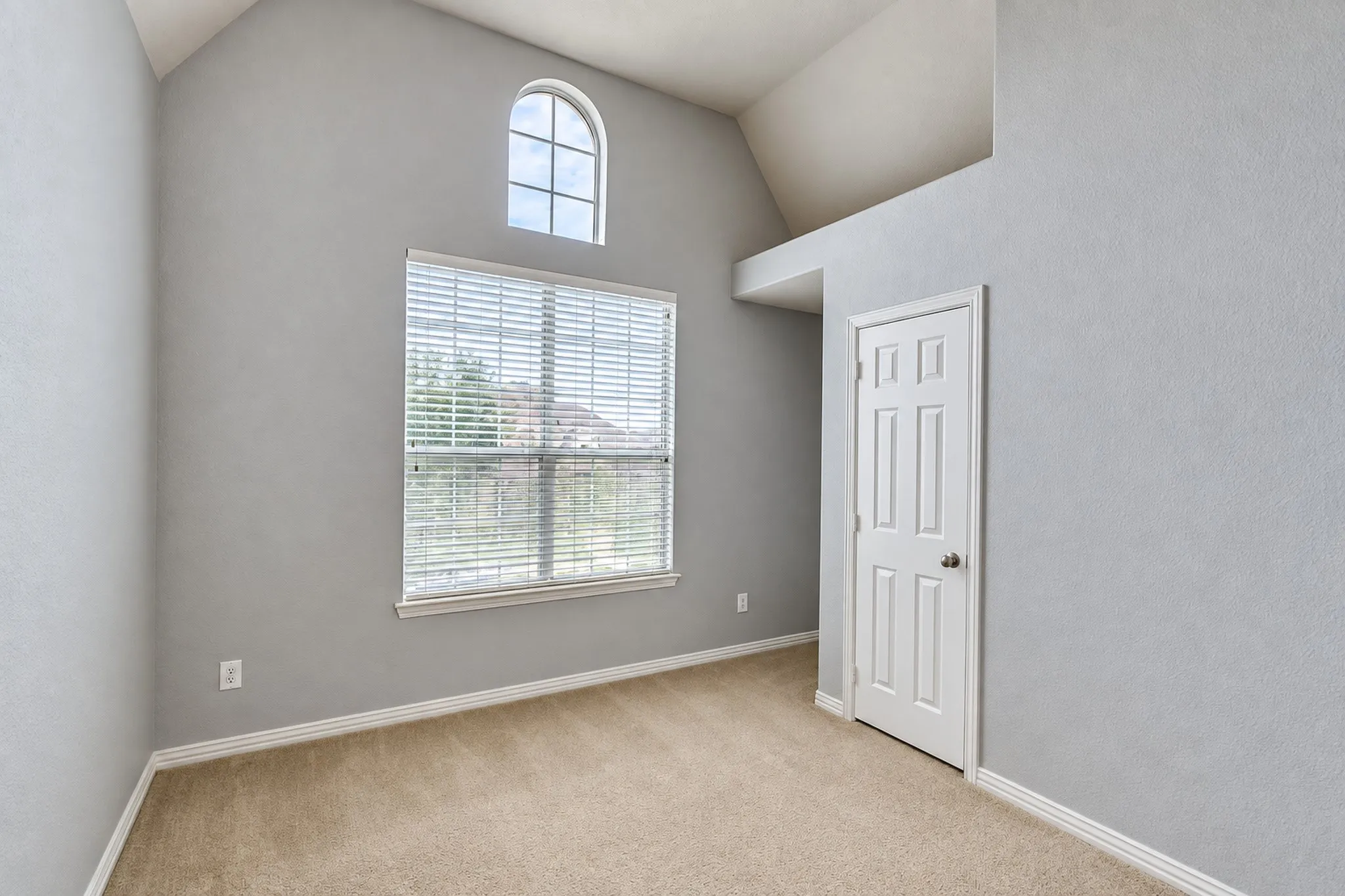 Arched window, vaulted ceiling, and neutral carpet flooring