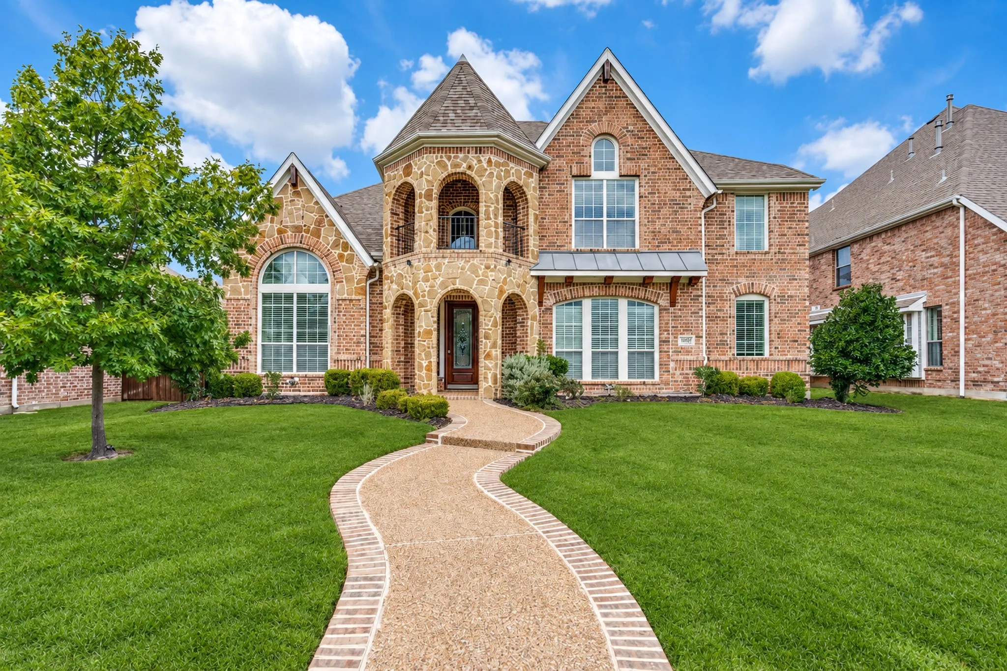 Brick and stone exterior with arched windows, a curved walkway, and a prominent turret feature