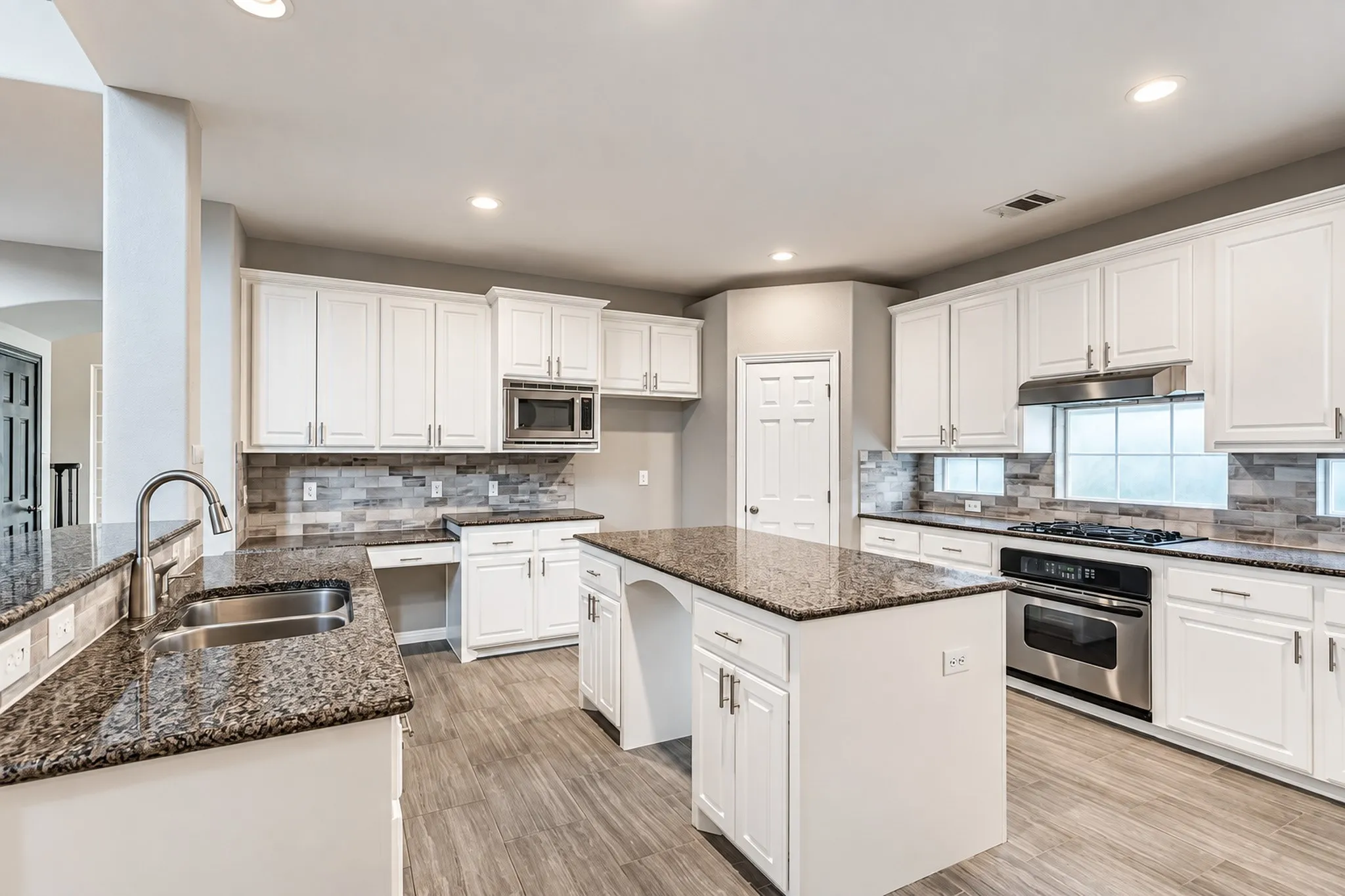 Kitchen featuring wood-finish flooring, white cabinetry, a central island with a granite countertop, stainless steel appliances, and a tile backsplash