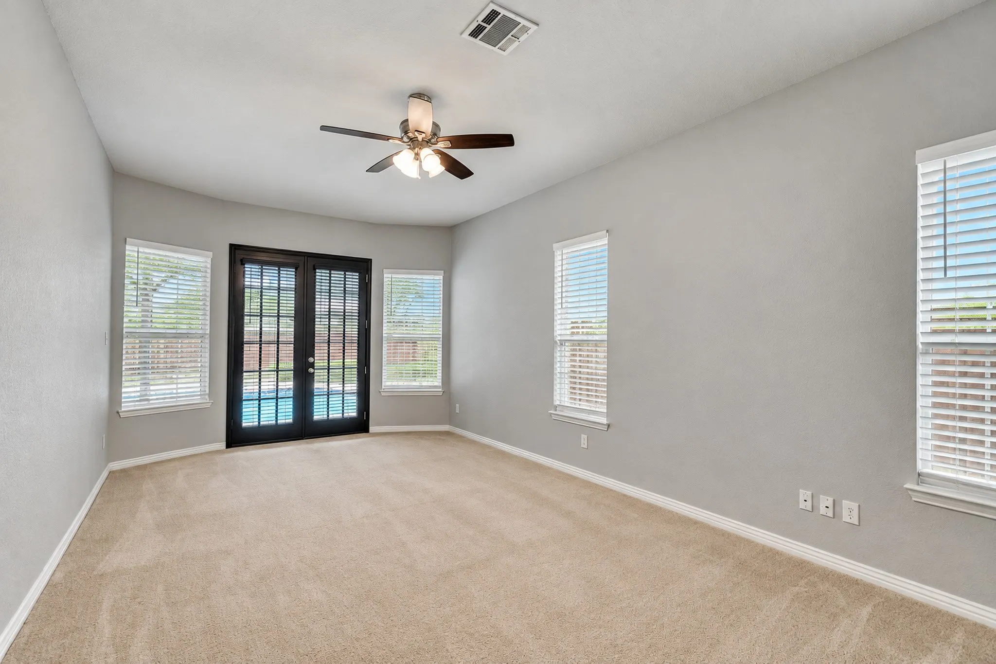 Carpeted interior space with a ceiling fan, multiple windows, and exterior double doors