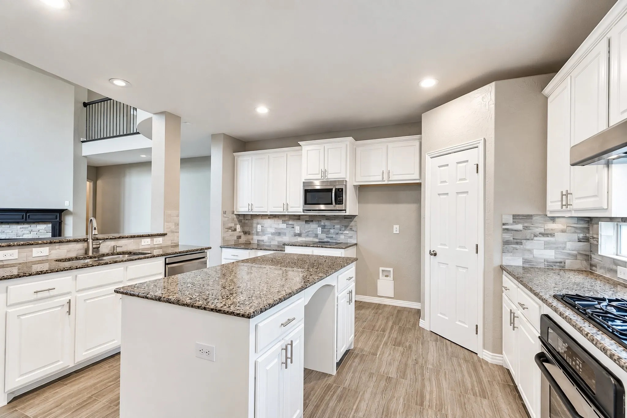 Gourmet kitchen featuring a central island, wood-finish flooring, white cabinetry, integrated stainless steel appliances, and stone countertops