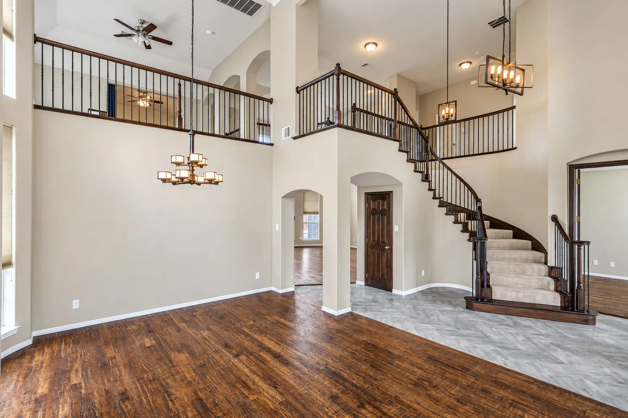 Two-story ceiling, wood-finish flooring, curved staircase with carpeted treads, wrought iron balusters, and recessed lighting