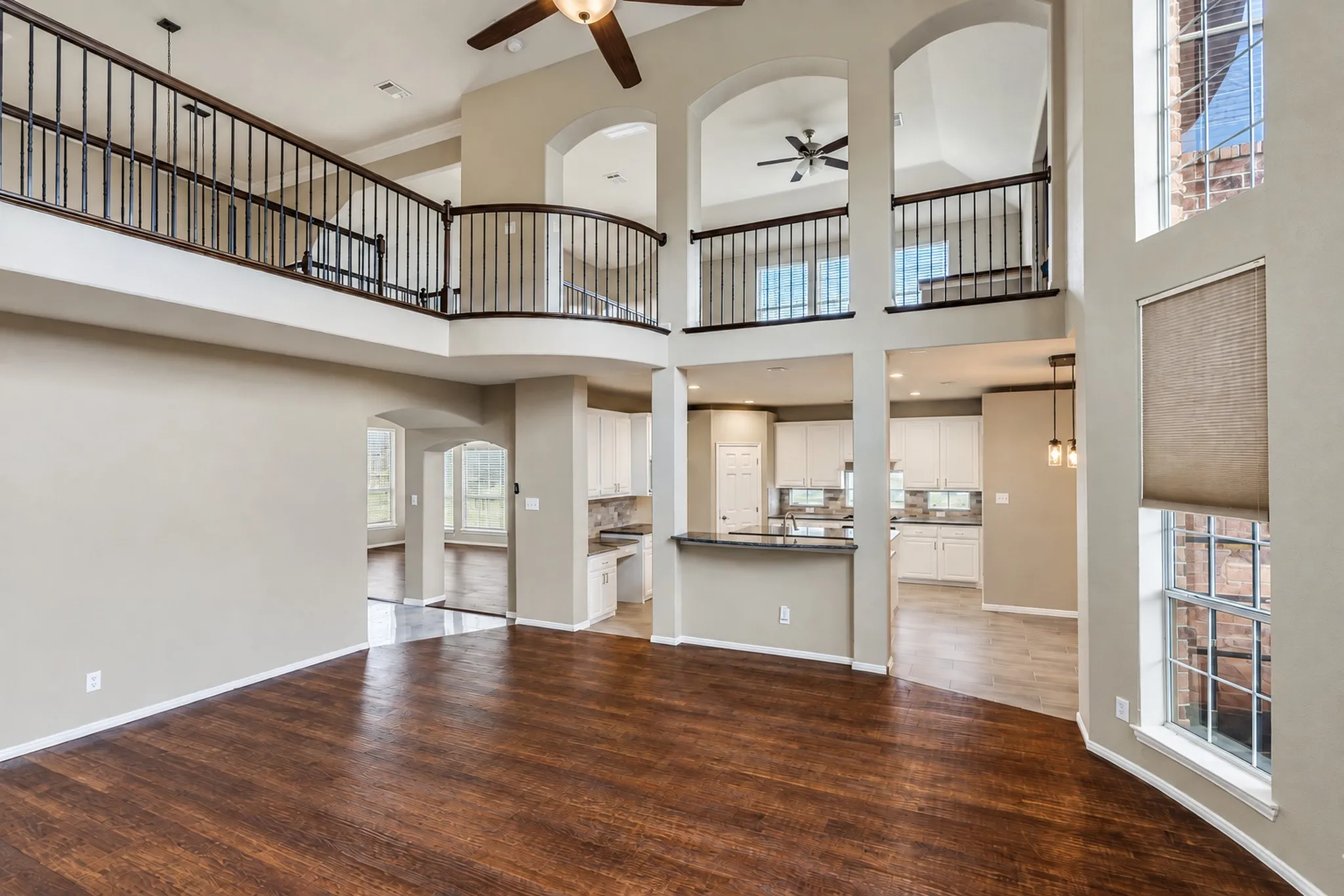 Expansive high ceilings with a second-story balcony featuring wrought iron railings, wood-finish flooring, and arched doorways