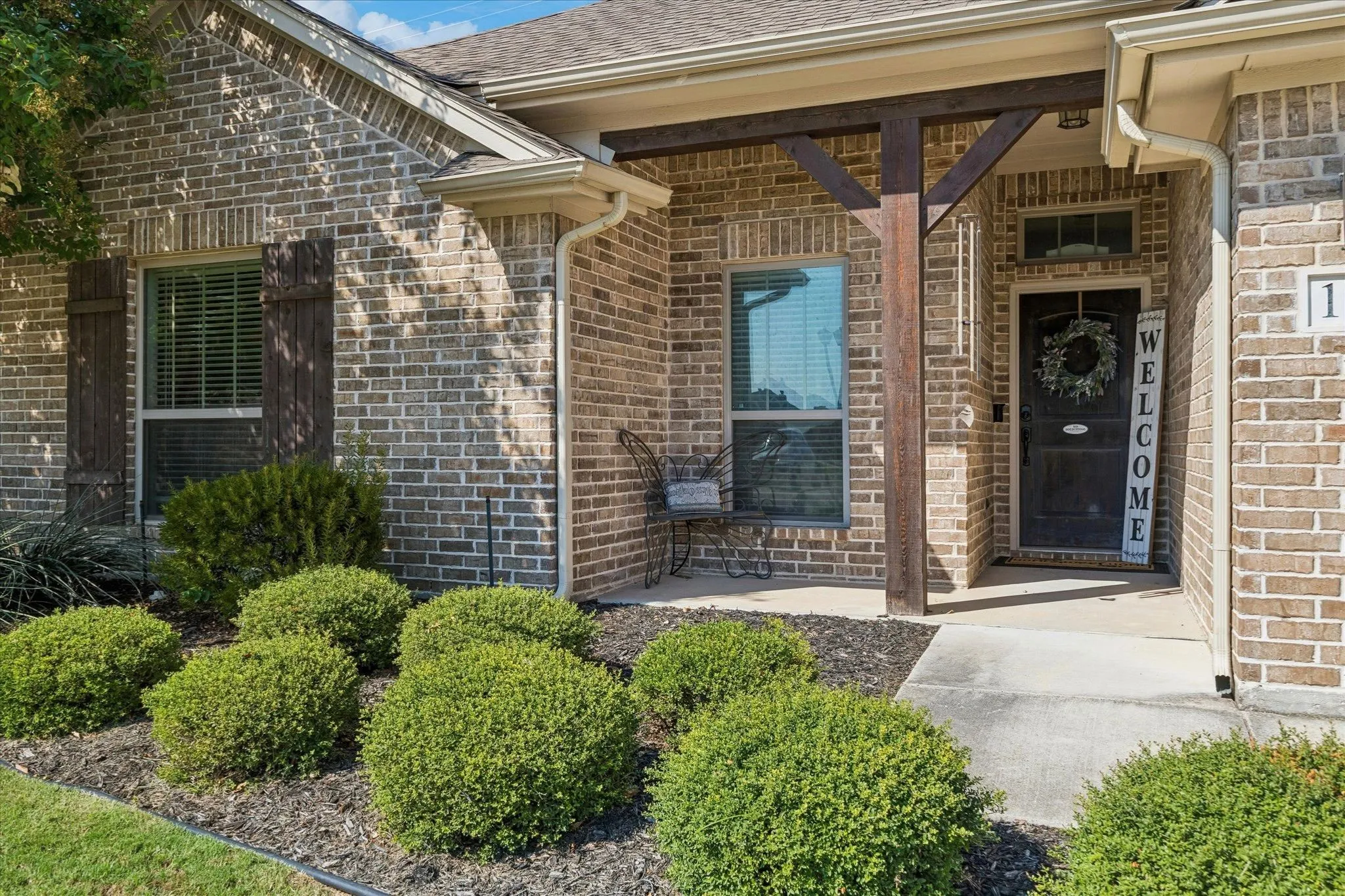 Brick exterior with wood shutters, covered entry with timber beam accents, and mature front landscaping