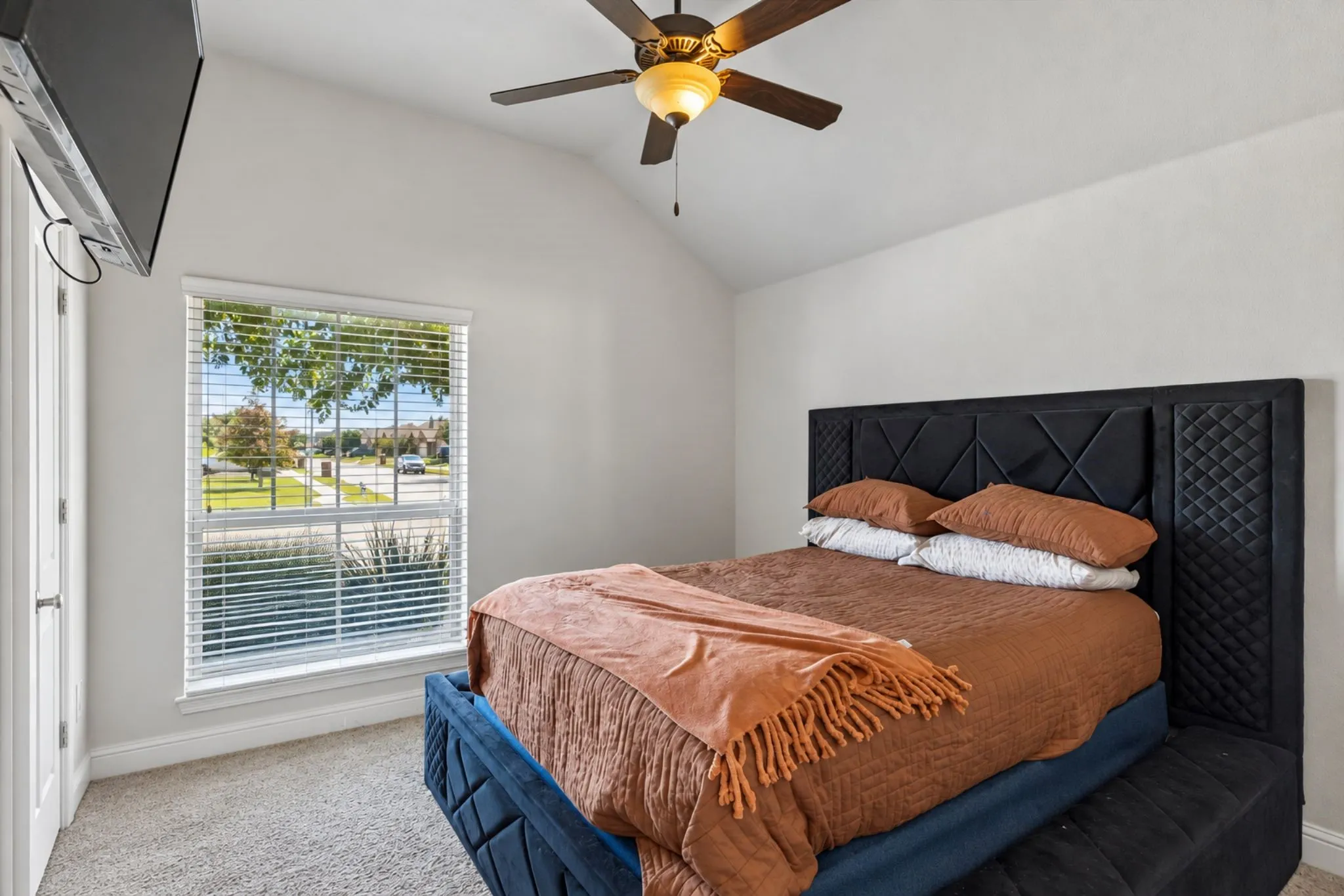 Vaulted ceiling, ceiling fan with integrated lighting, large window with blinds, and neutral carpet flooring