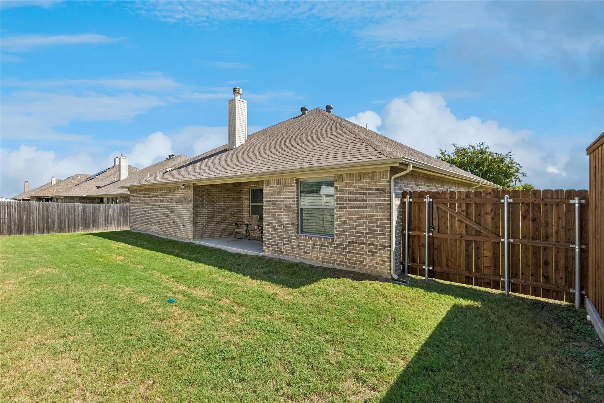 Brick exterior, covered patio, shingle roof, wood privacy fence, and a gate