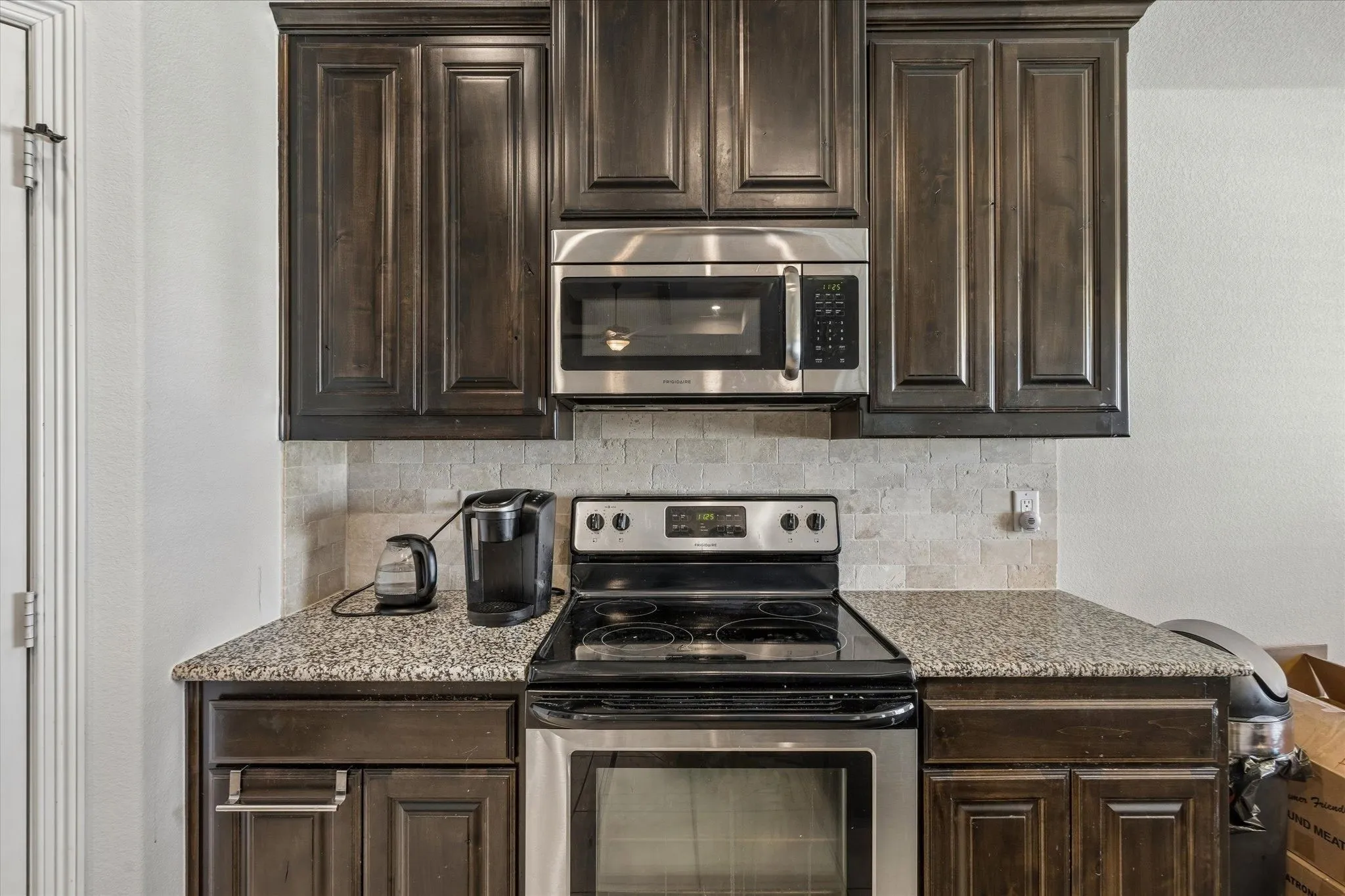Stainless steel range and microwave oven, granite-finish countertops, and classic wood cabinetry with crown molding, complemented by a tiled backsplash
