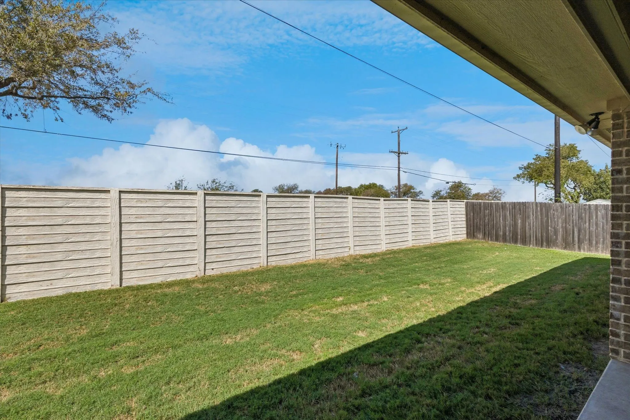 Expansive grass yard with a concrete panel fence and a wood plank fence