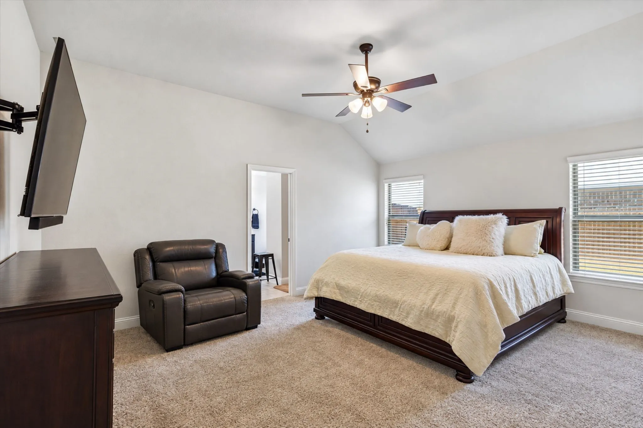 Vaulted ceiling with a ceiling fan, carpeted flooring, and window treatments on multiple windows