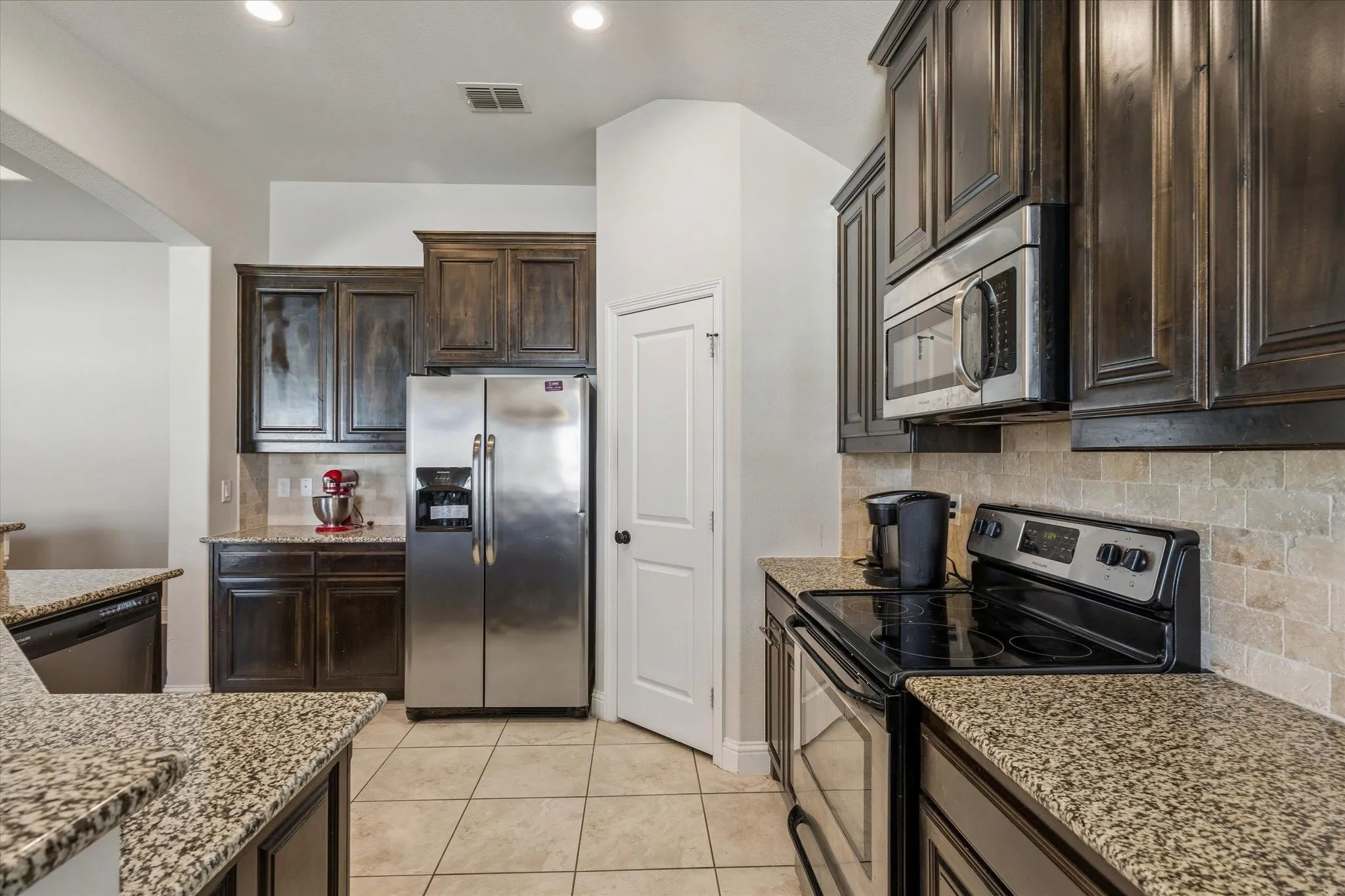 Kitchen featuring granite countertops, dark wood-finish cabinetry, stainless steel appliances, and tile flooring