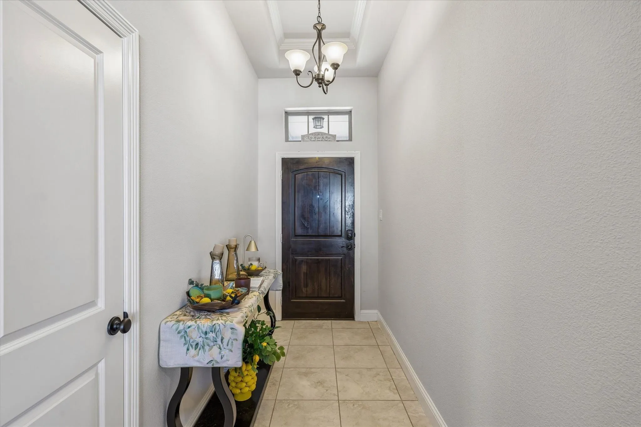 Arched wood-panel entry door with transom window, tile flooring, and a decorative ceiling light fixture