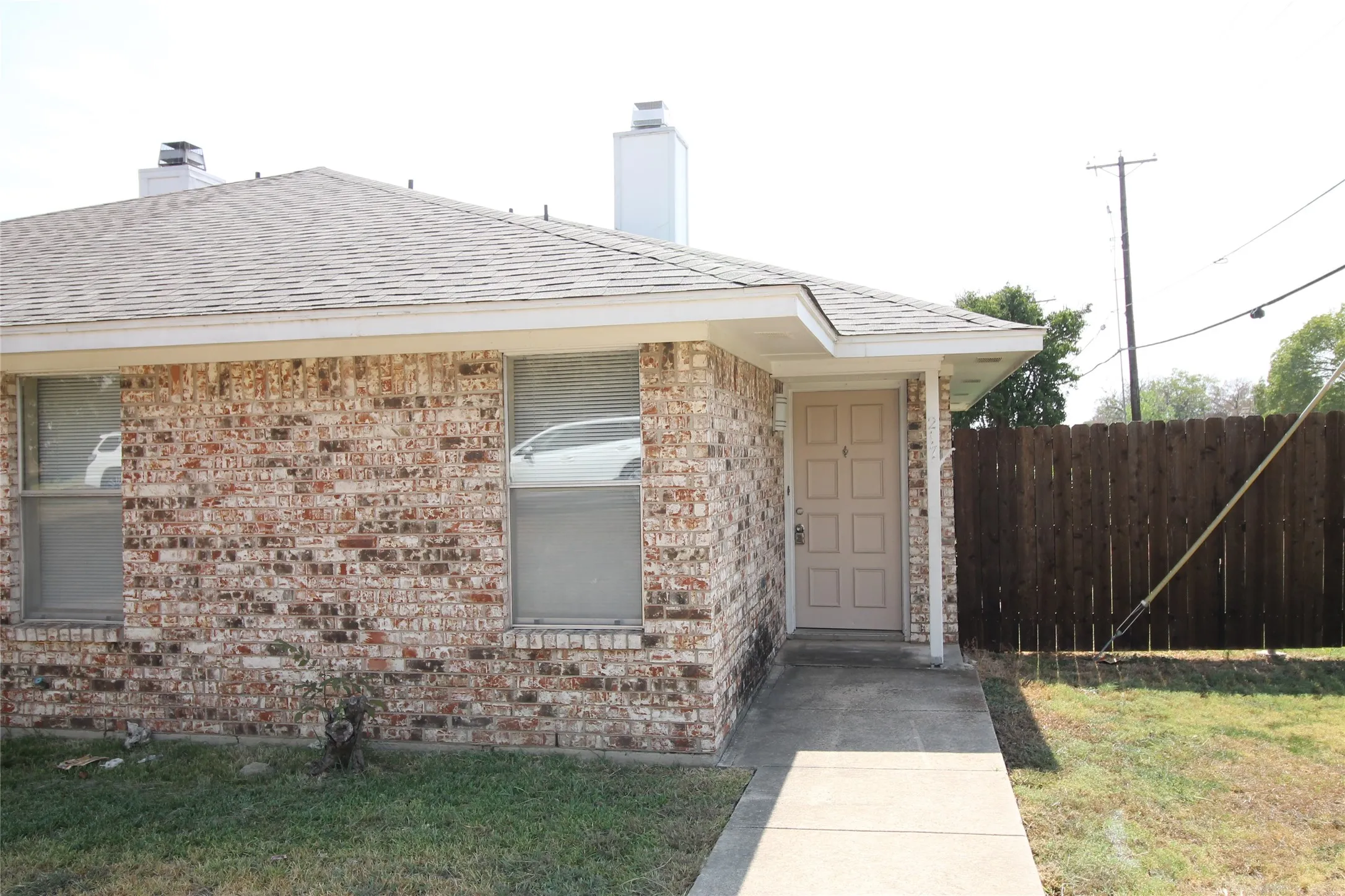 Brick exterior with a peaked roof, concrete walkway, and a paneled front door