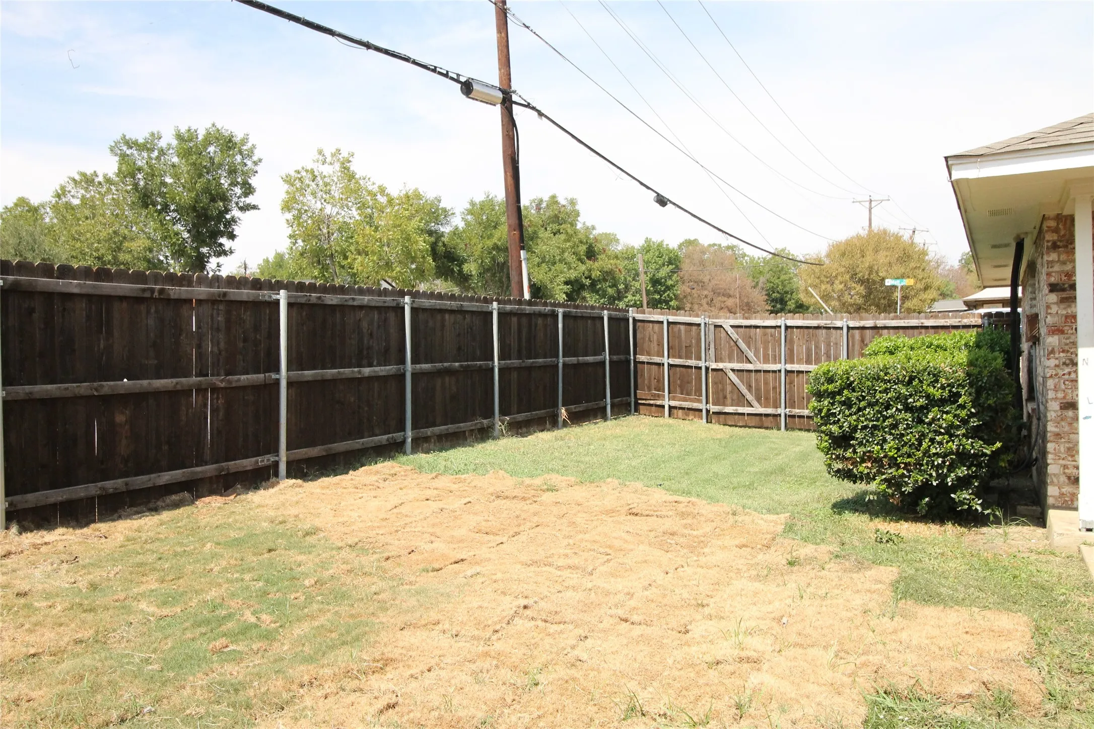 Fenced backyard with a wood privacy fence, a wood fence gate, and established shrubbery