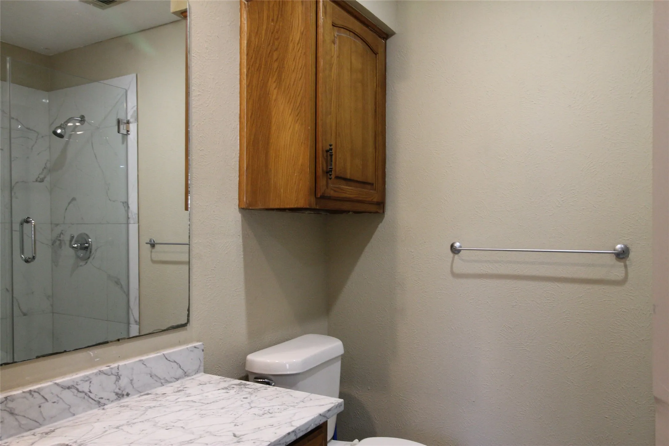 Glass-enclosed shower with a rainfall showerhead, white and gray veined tile, and a built-in shower niche