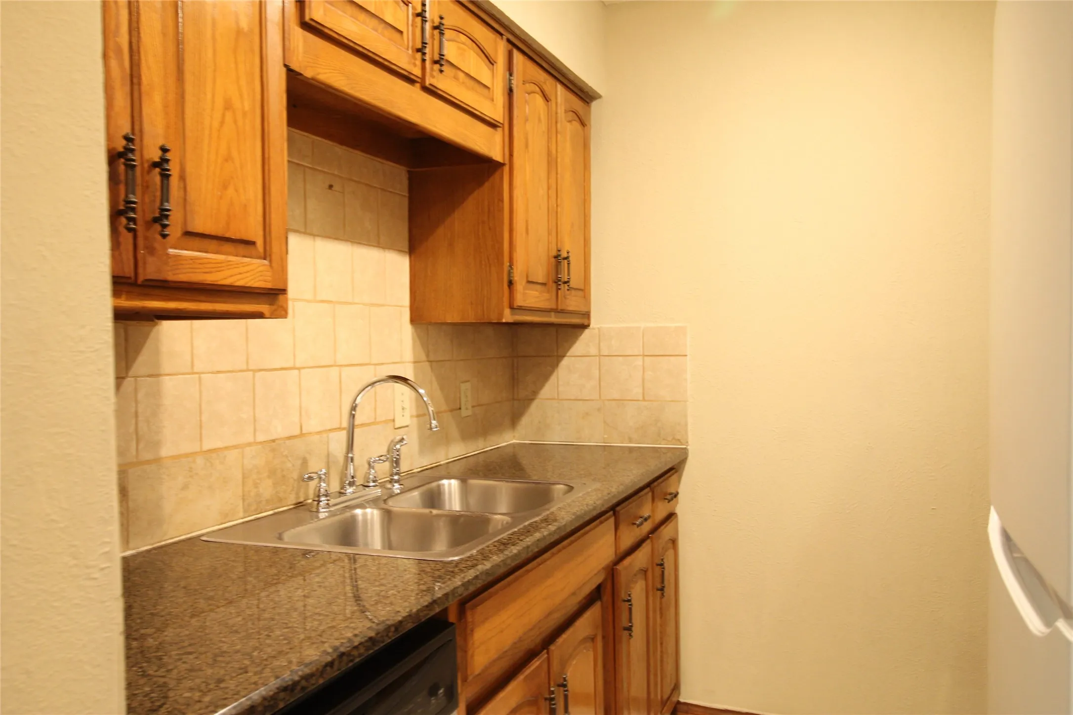 Wood cabinetry with dark hardware, dual basin stainless steel sink, chrome faucet, and tiled backsplash