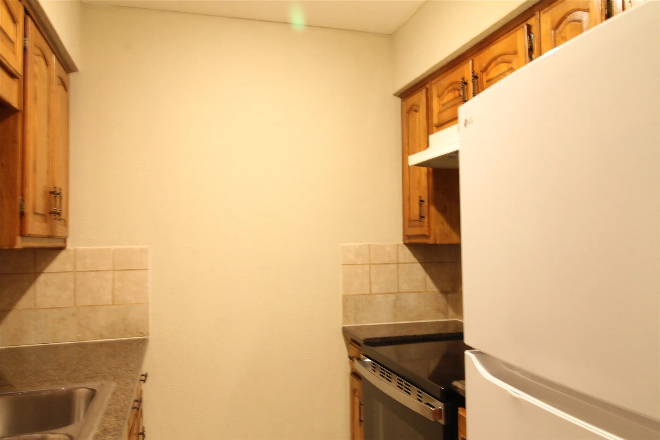 Kitchen featuring wood-finish cabinetry, tile backsplash, built-in range, and a refrigerator