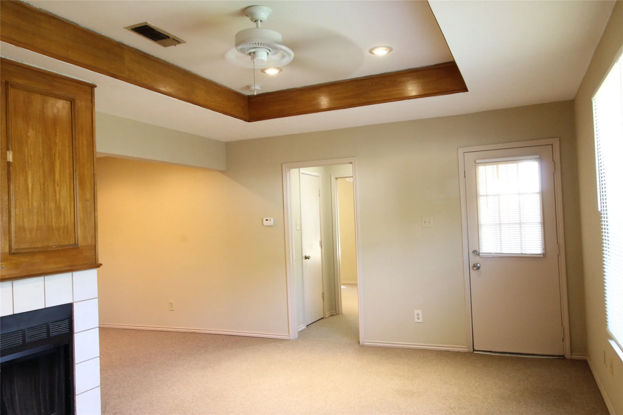 Living space featuring a tray ceiling with wood-finish trim, recessed lighting, a ceiling fan, and a fireplace with white tile surround