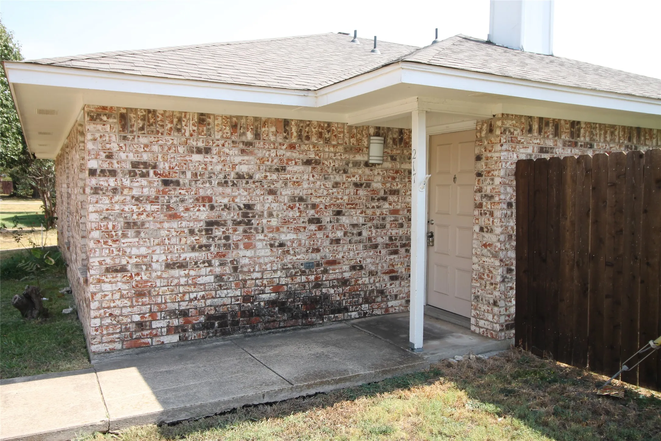 Brick exterior with covered entryway, concrete walkway, and privacy fence