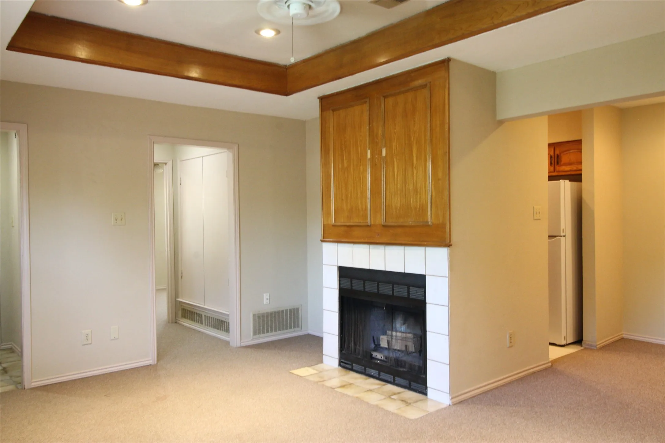 Carpeted living area featuring a fireplace with white tile surround, wood-finish cabinetry, and recessed lighting
