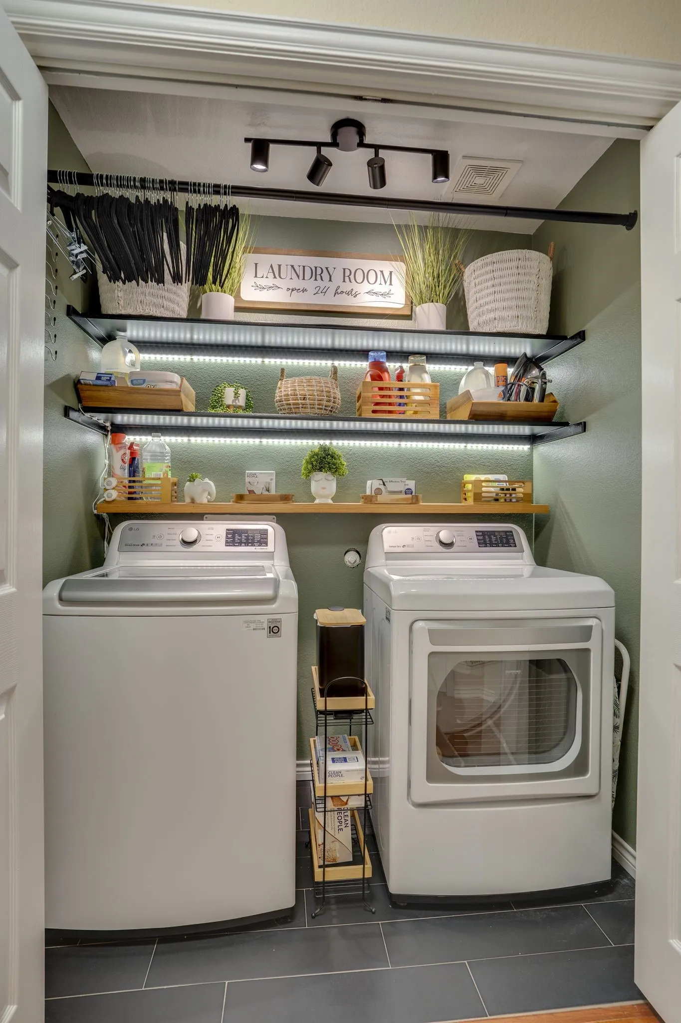 Compact laundry area featuring dark tile flooring, track lighting, and built-in shelving with integrated lighting