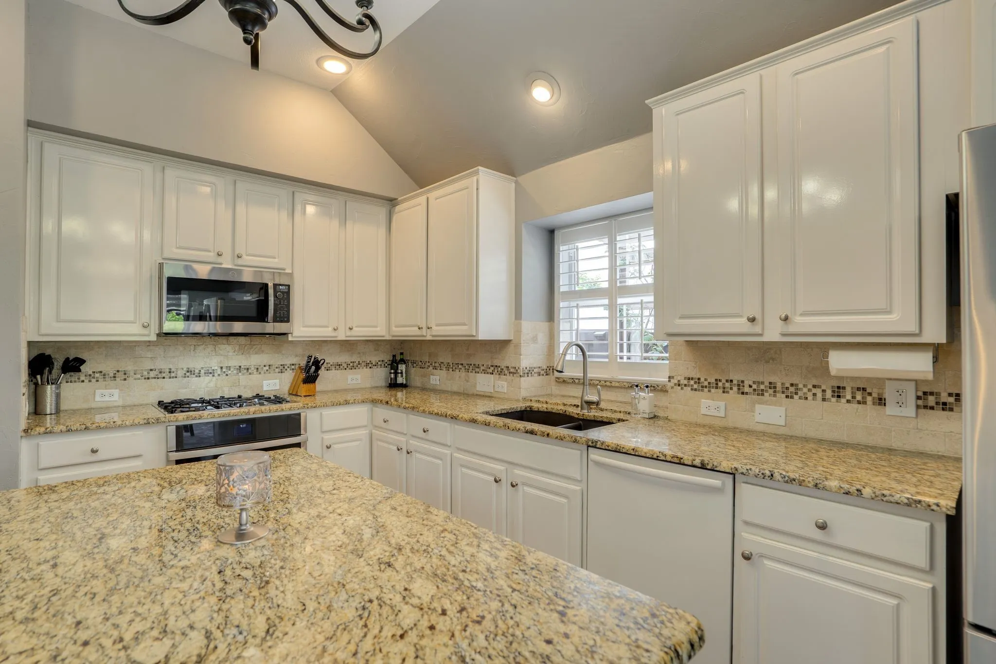 Kitchen featuring white cabinetry, granite countertops, tile backsplash, and stainless steel appliances
