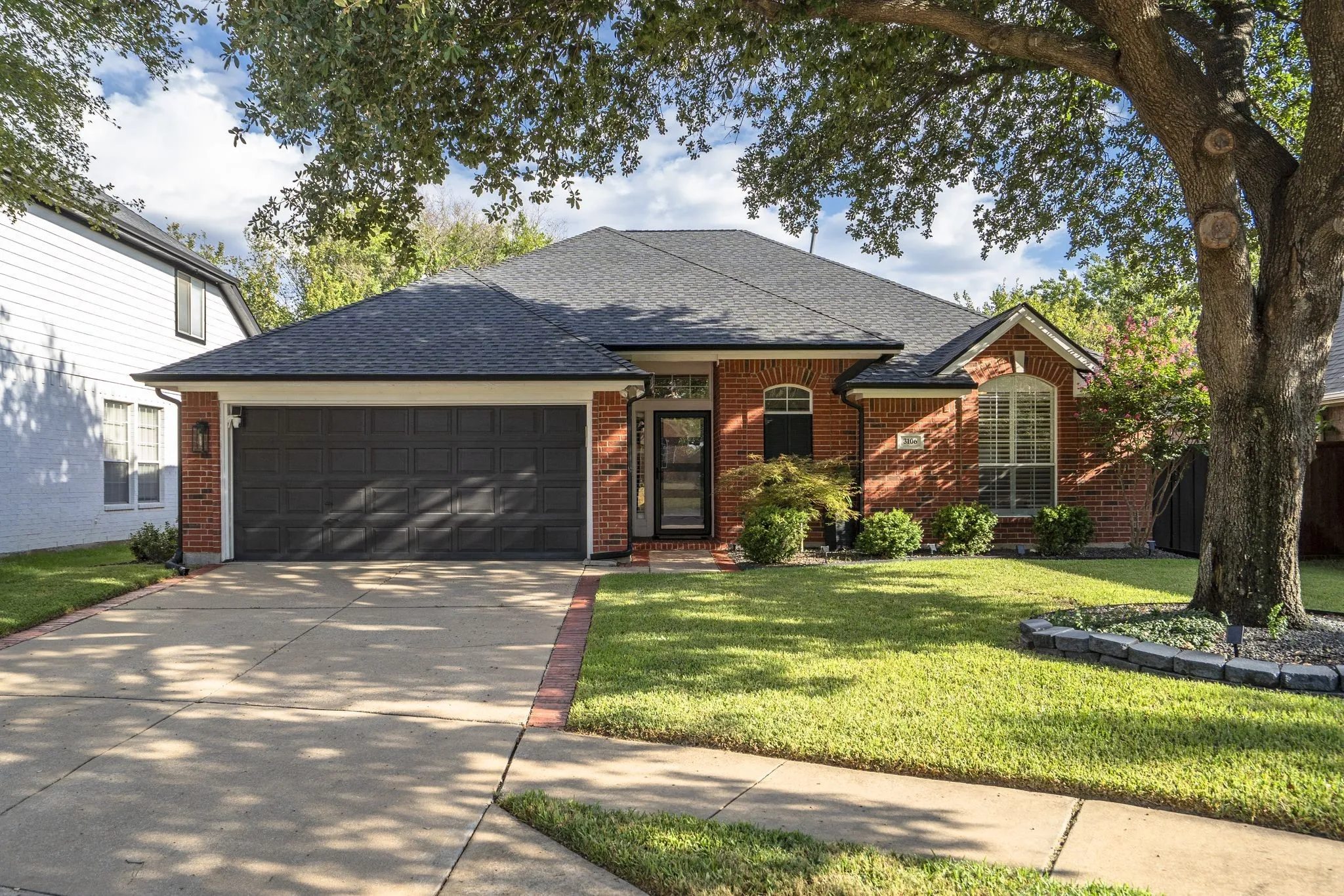 Brick facade with an arched entry, dark gray garage door, and a concrete driveway with brick accents