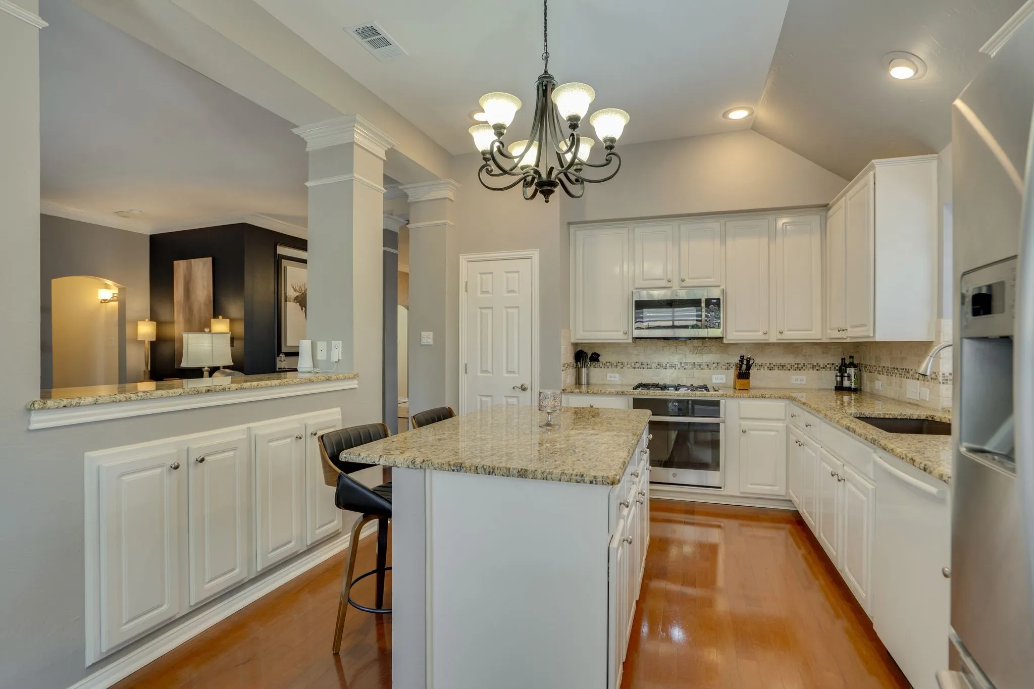 Kitchen featuring an island with stone countertop, white cabinetry, stainless steel appliances, and wood-finish flooring