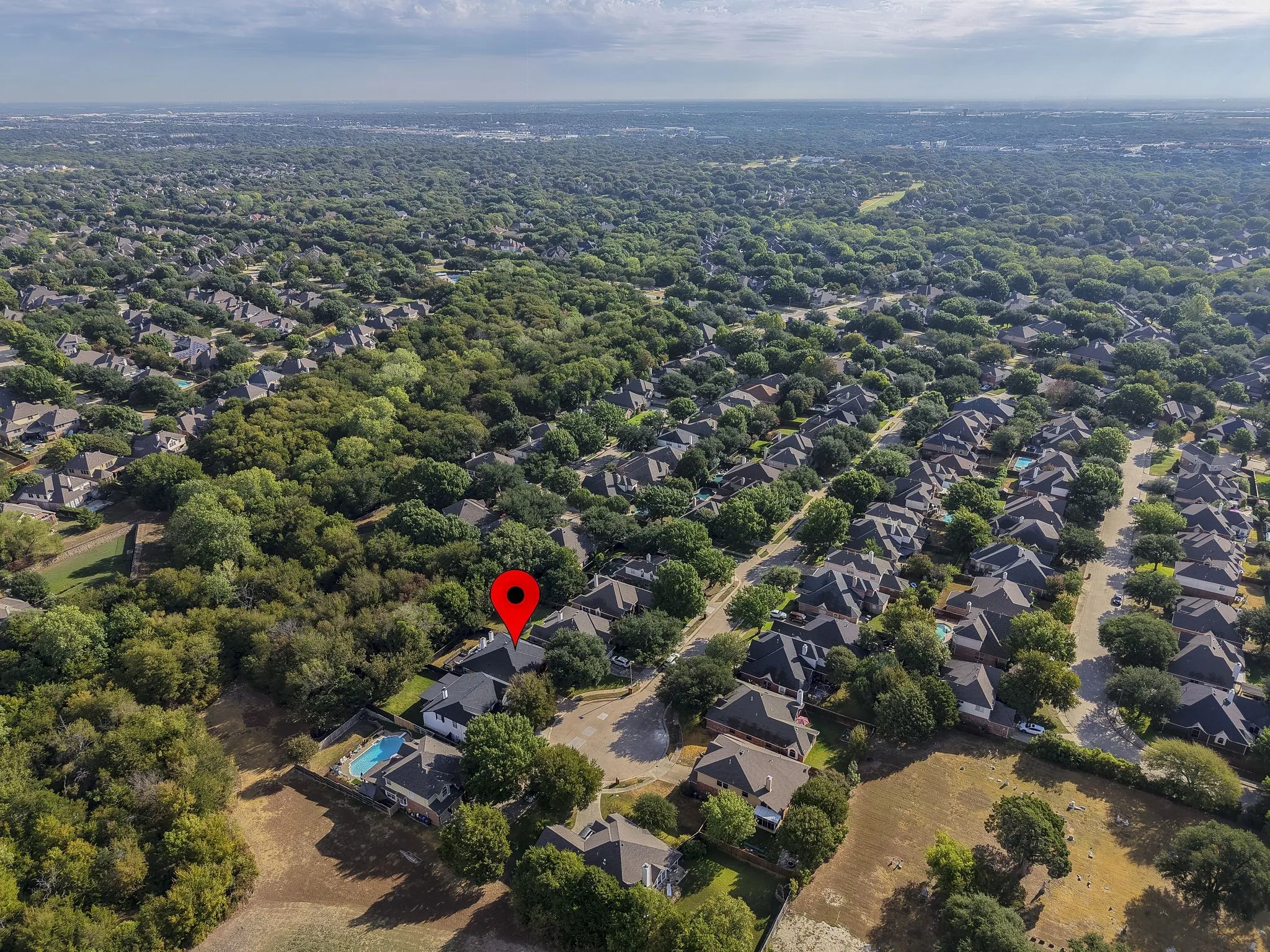 Aerial overview of a residential area featuring numerous single-family homes, mature tree cover, and a private pool