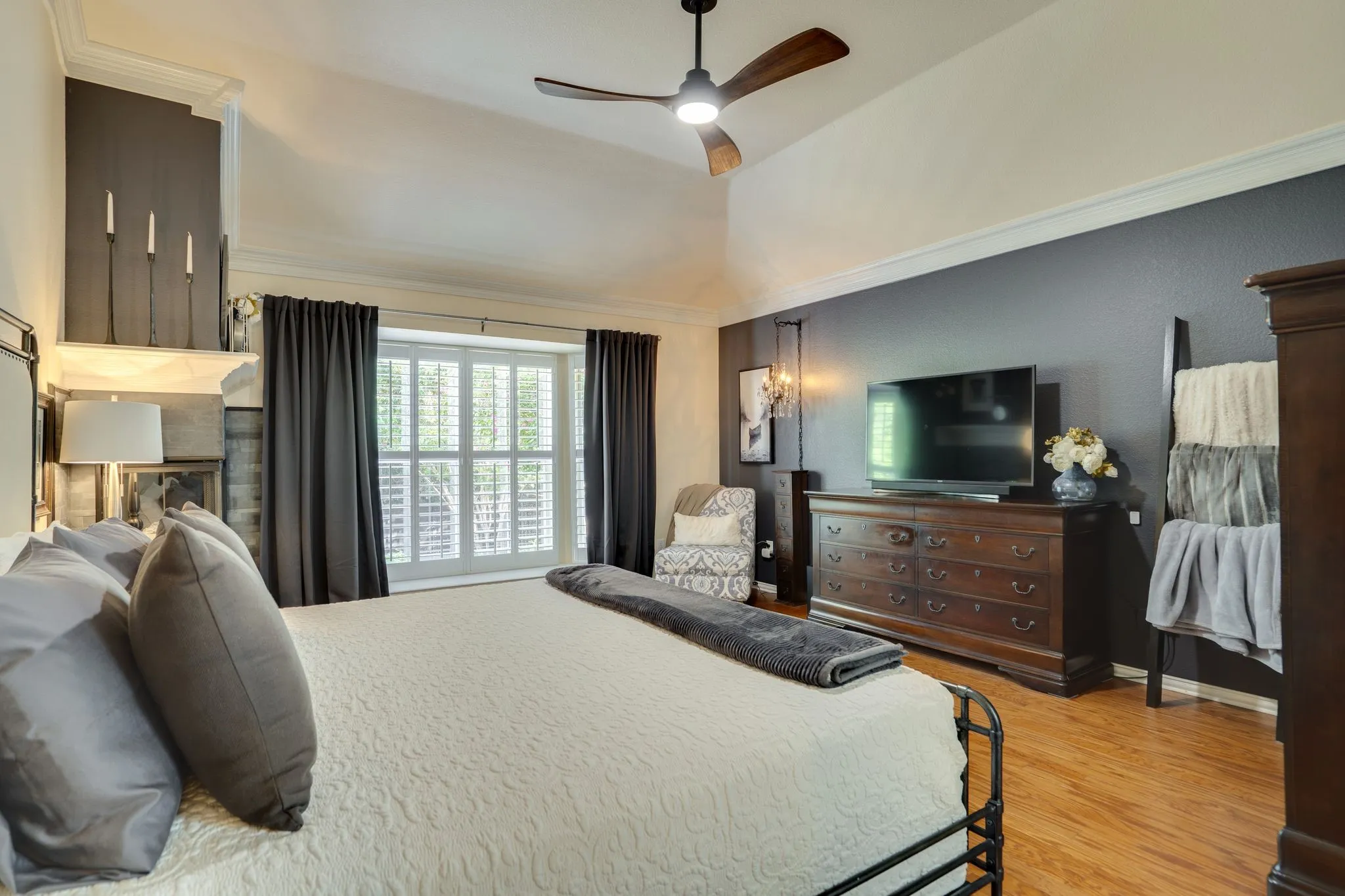 Vaulted ceiling with a ceiling fan, window with plantation shutters, wood-finish flooring, and crown molding