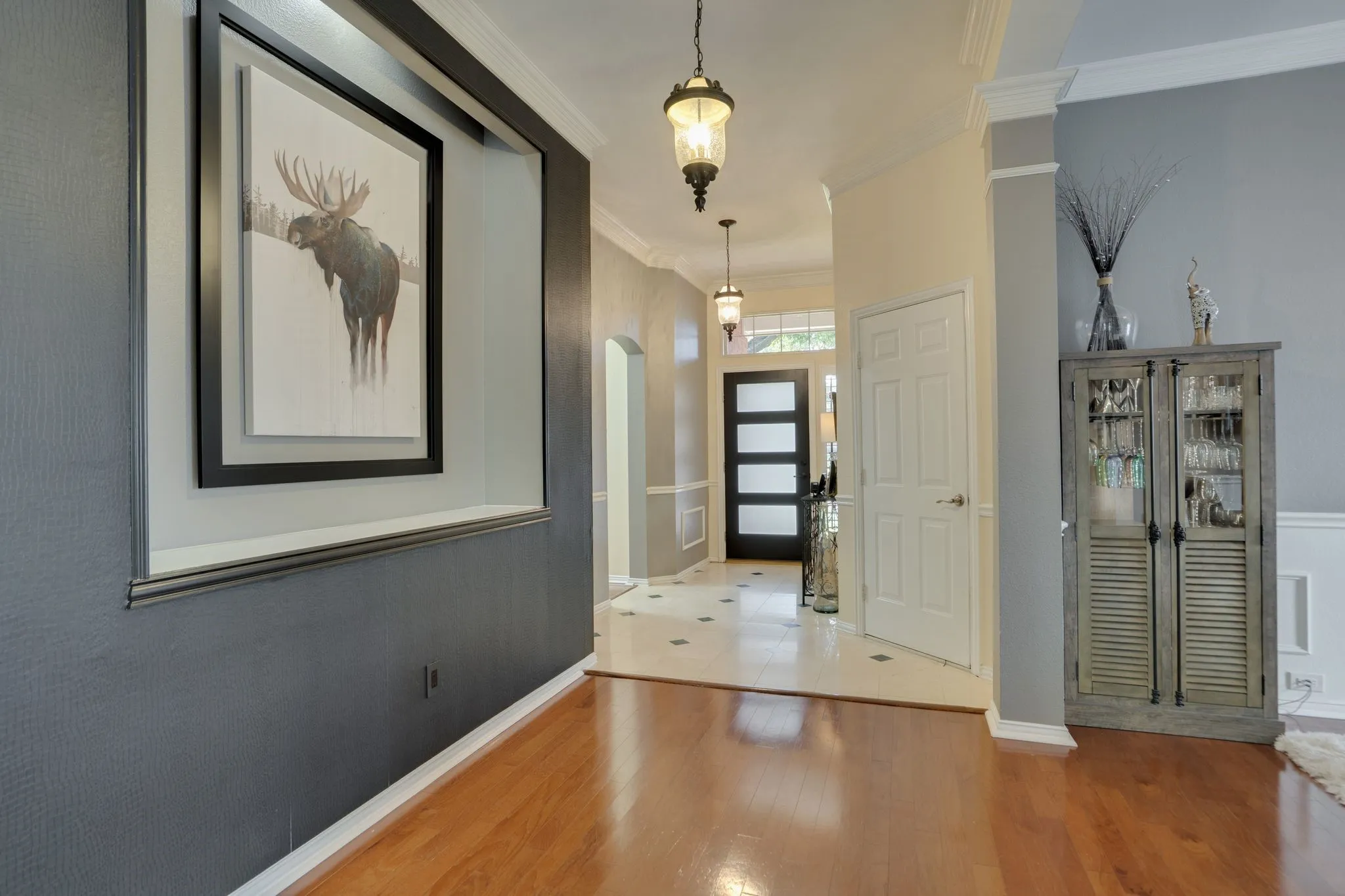 Wood-finish flooring, recessed wall niche, two-tone wall treatment, crown molding, and a paneled entry door with frosted glass inserts