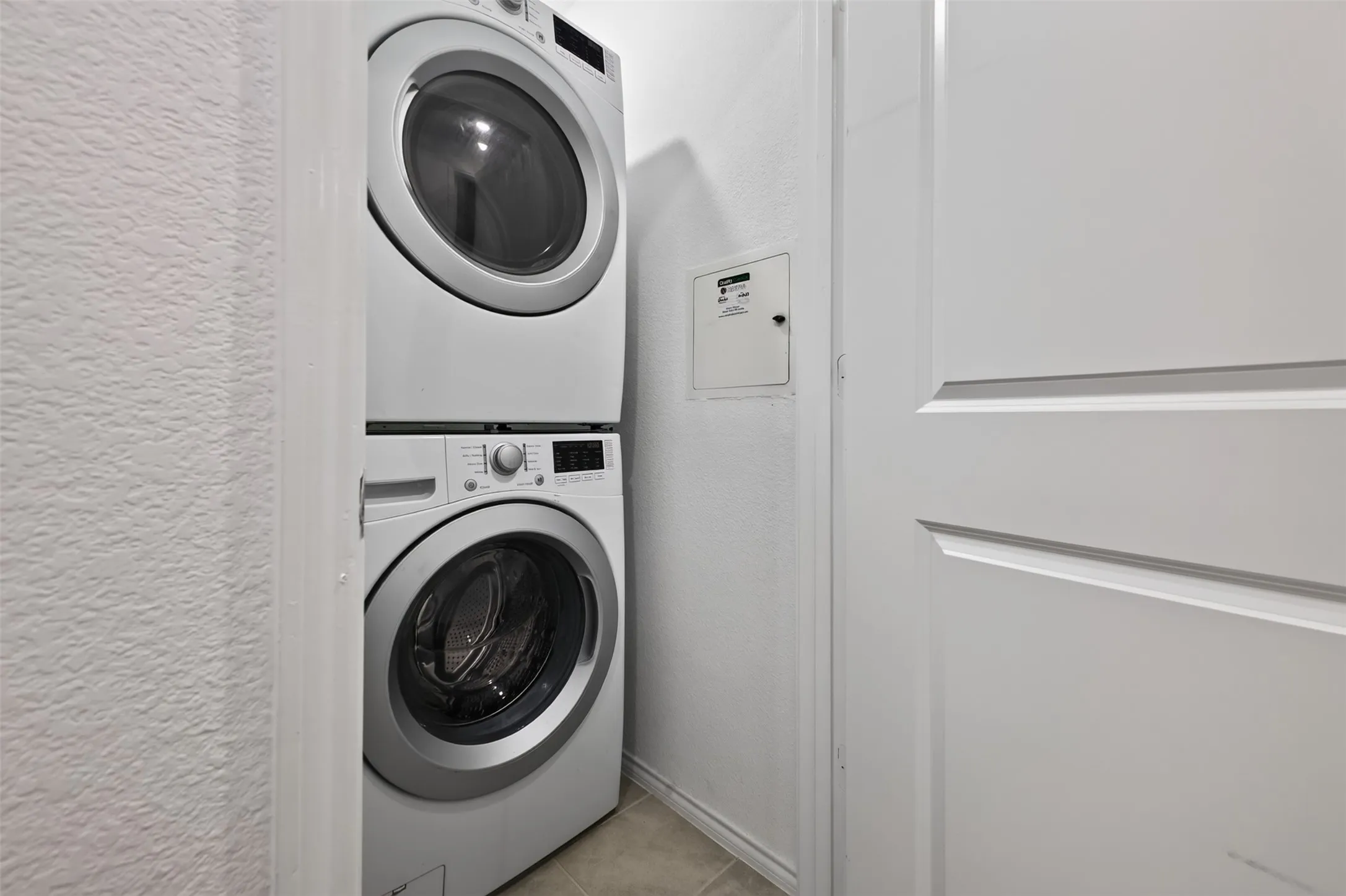 Stackable white washer and dryer units, white paneled interior door, and light-toned floor tiling