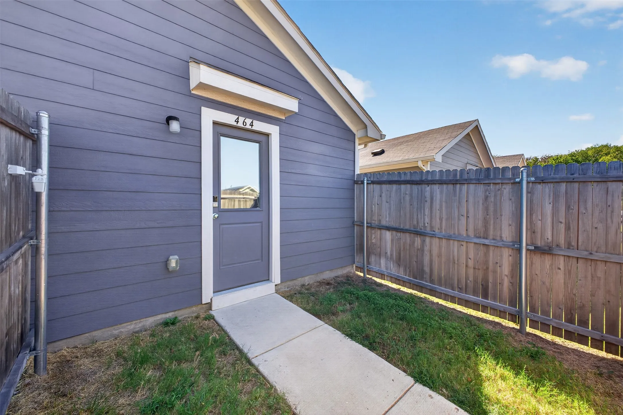 Siding exterior with a gable roof, featuring a single entry door with an overhead light fixture