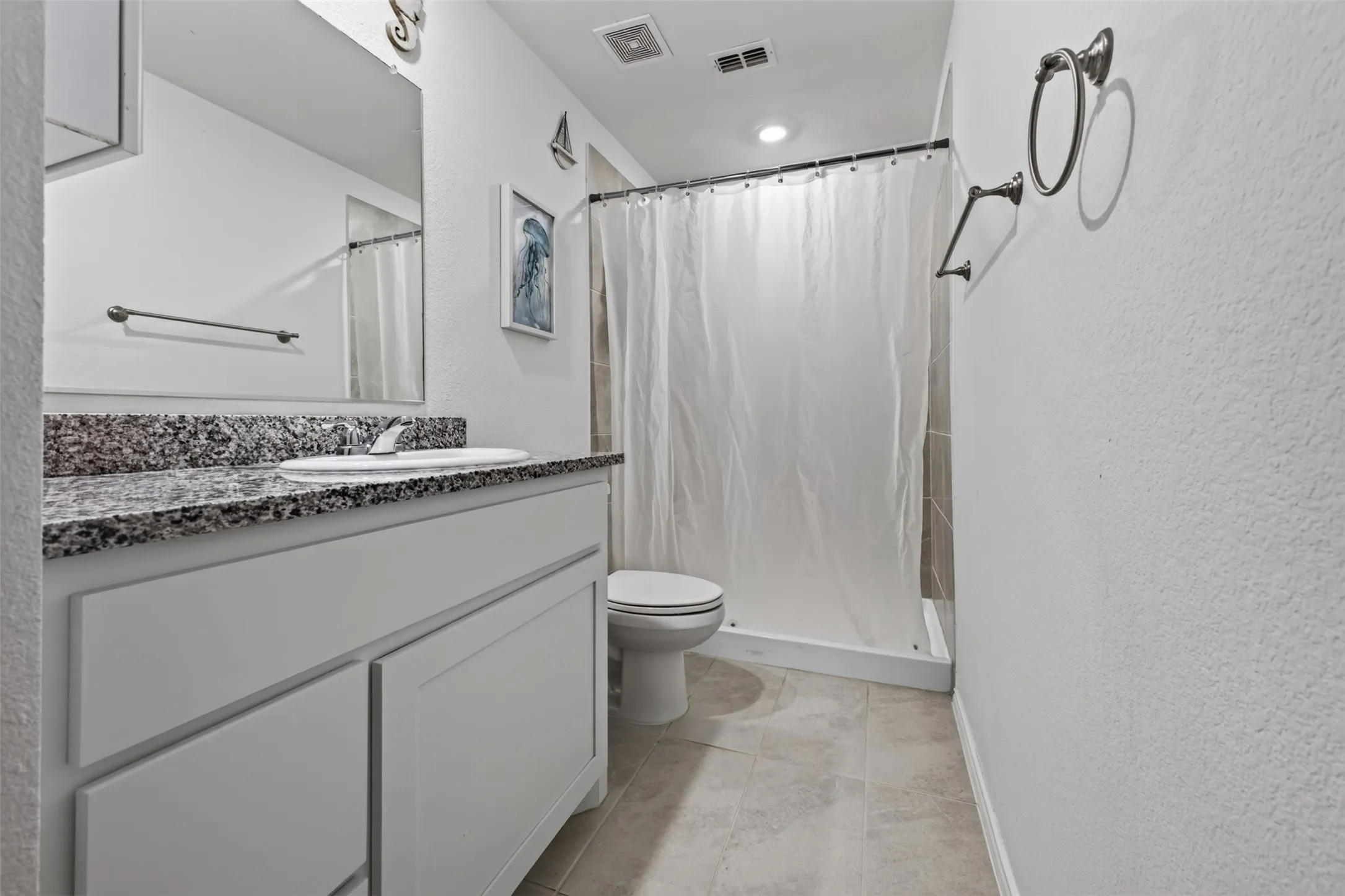 White vanity with a speckled countertop, undermount sink, and wall-mounted mirror