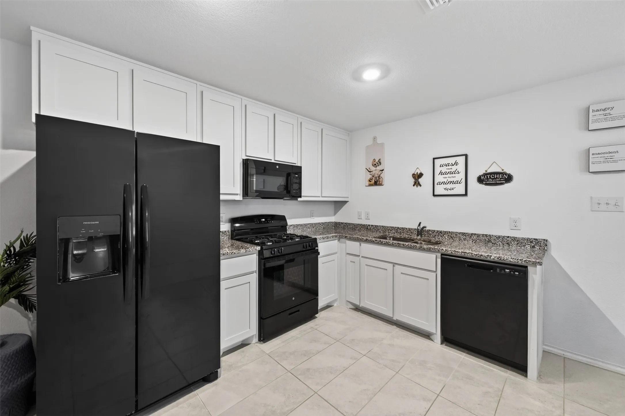 White shaker-style cabinetry, dark speckled countertops, stainless steel sink, black range with an overhead microwave, and integrated black dishwasher