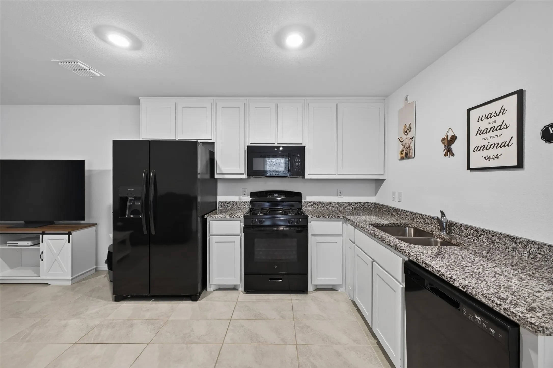 White cabinetry, black appliance suite, light-toned tile flooring, and speckled countertops