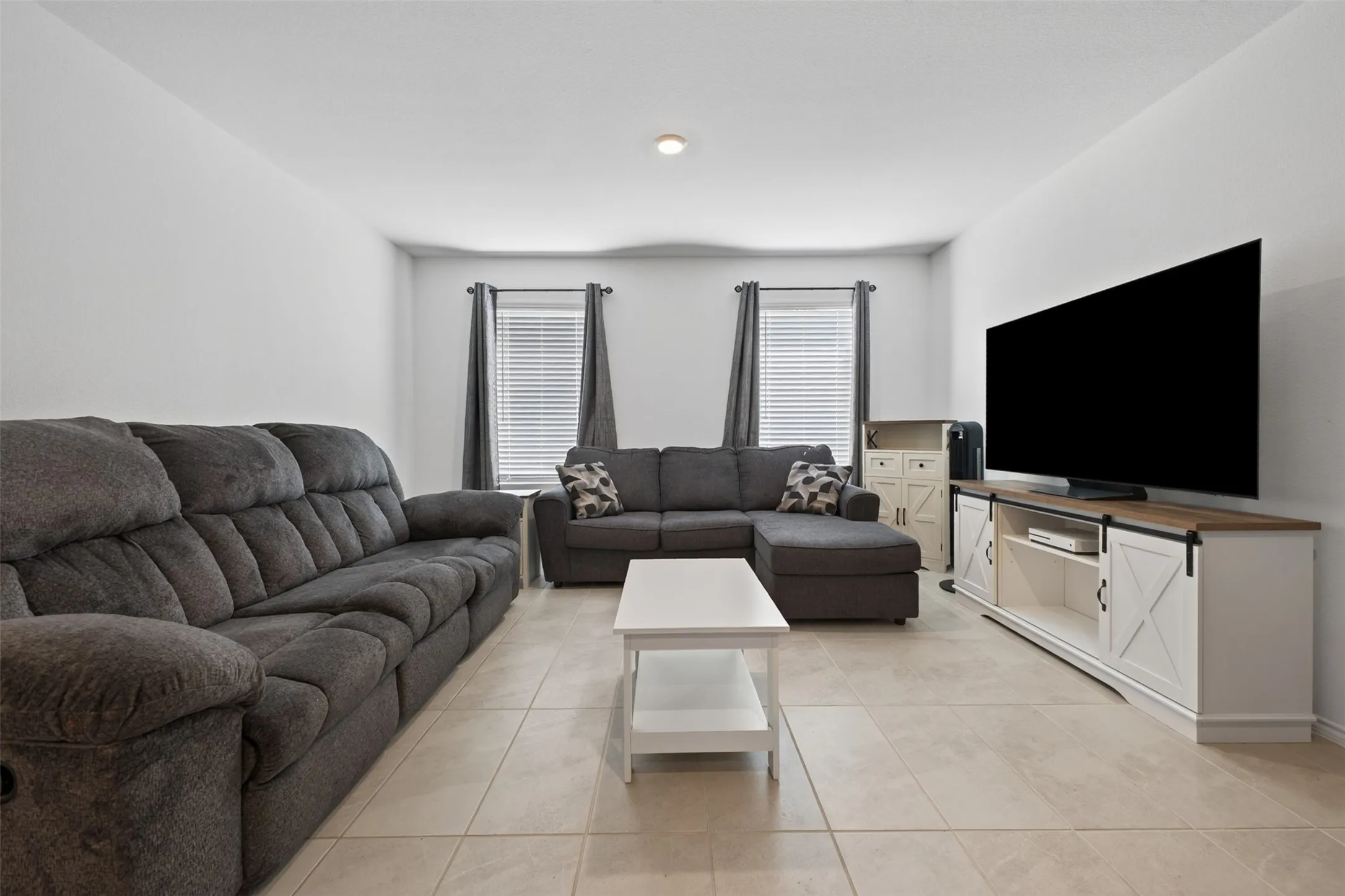 Recessed lighting, tile flooring, window with blinds, and white walls create a bright living space