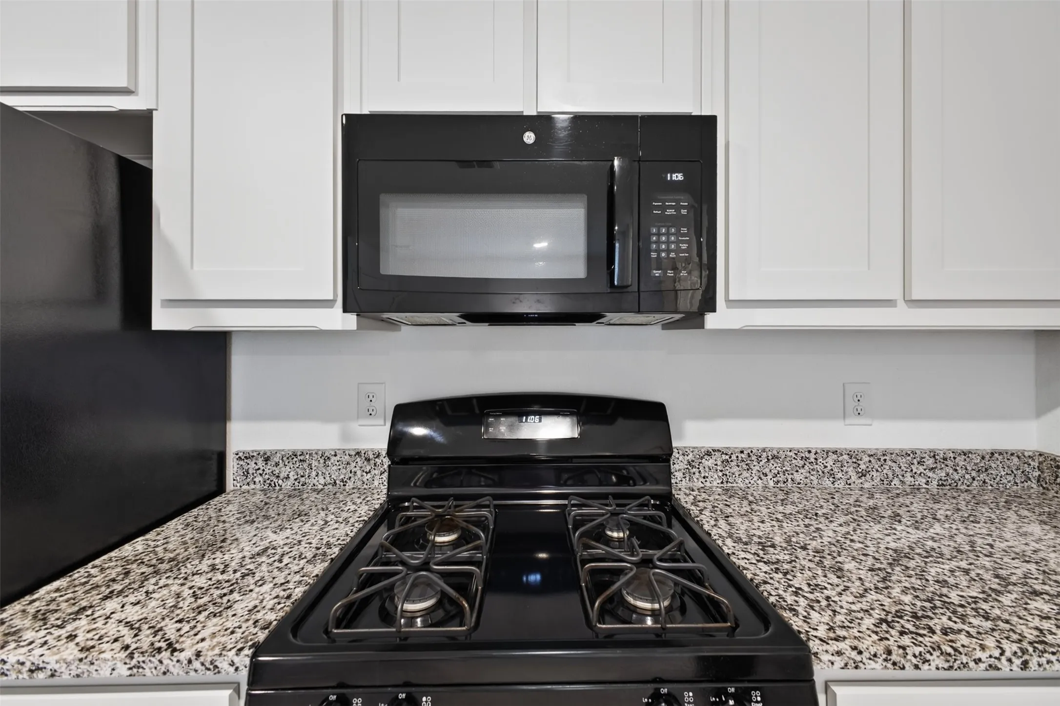 White cabinetry, black over-the-range microwave, black gas range, and speckled countertops