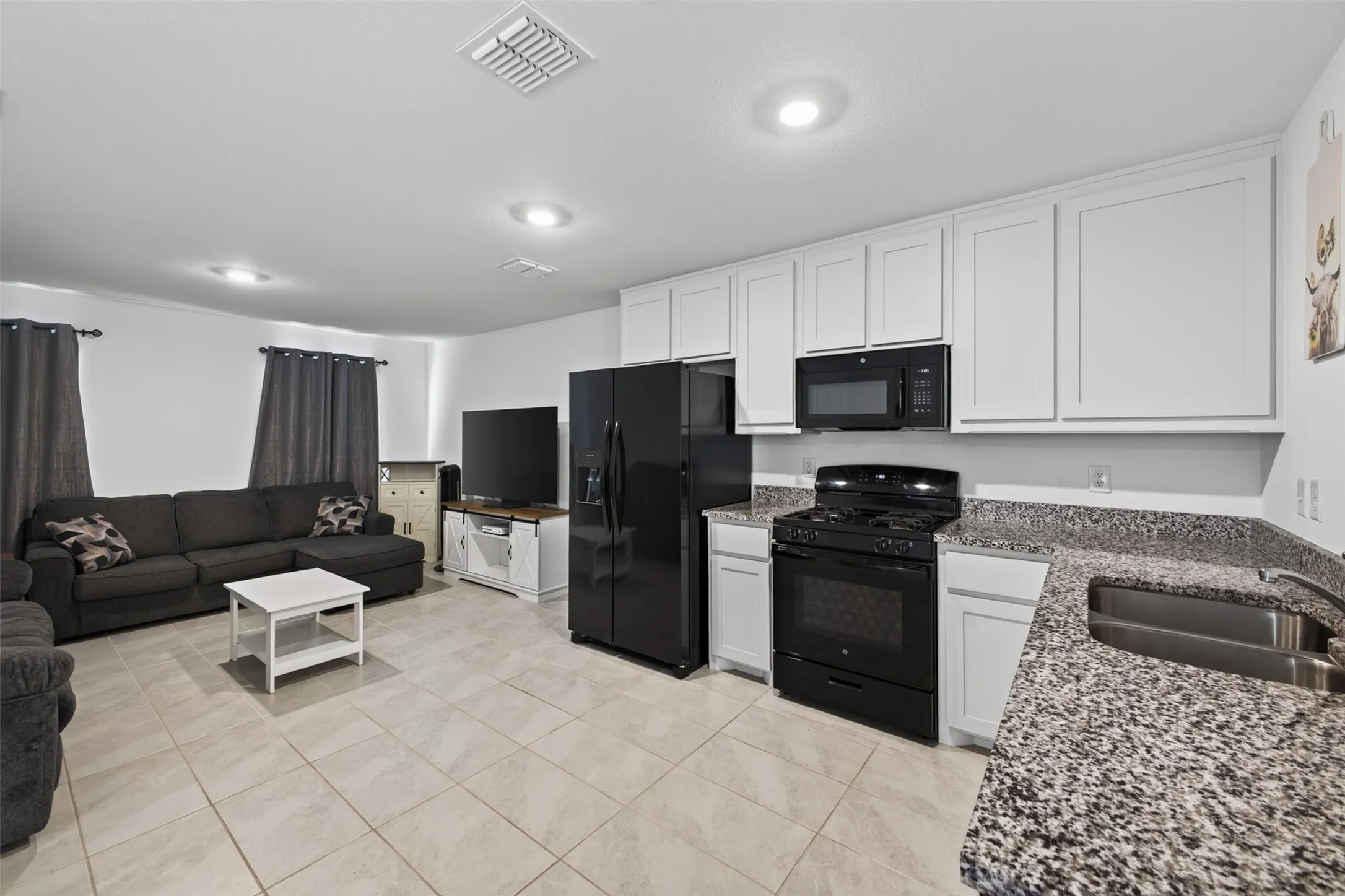 Open-concept living space featuring tiled flooring, recessed lighting, white cabinetry, speckled countertops, and black appliances